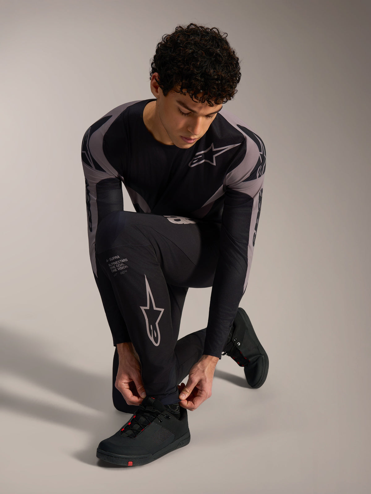 Zwarte Alpinestars A-Supra Elite-broek met grijze logo's, gedragen door een knielend model voor MTB-rijden.