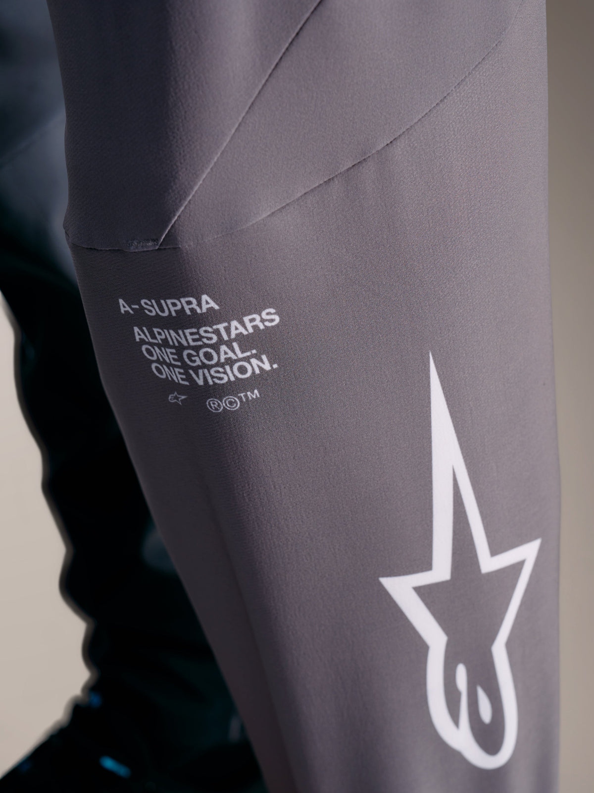 Pantalon A-Supra Elite gris dégradé avec marquage Alpinestars blanc et slogan "One Goal. One Vision."