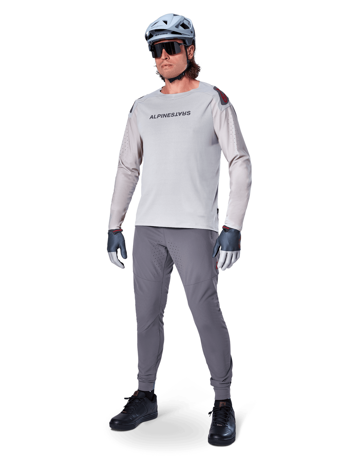 Pantalon Alpinestars A-Aria Elite, pantalon de VTT gris foncé, porté par un cycliste avec un maillot à manches longues gris clair et un casque gris, doté de ventilations découpées au laser sur les cuisses et d'une coupe performance ajustée pour le VTT