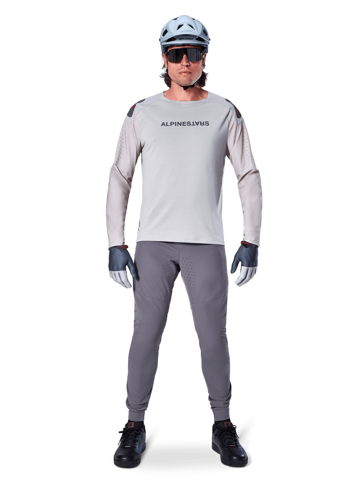 Pantalon Alpinestars A-Aria Elite, pantalon de VTT gris foncé, porté par un cycliste en maillot à manches longues gris clair, casque bleu clair et chaussures noires, doté de perforations laser visibles à l'intérieur des jambes et d'une coupe performance ajustée.