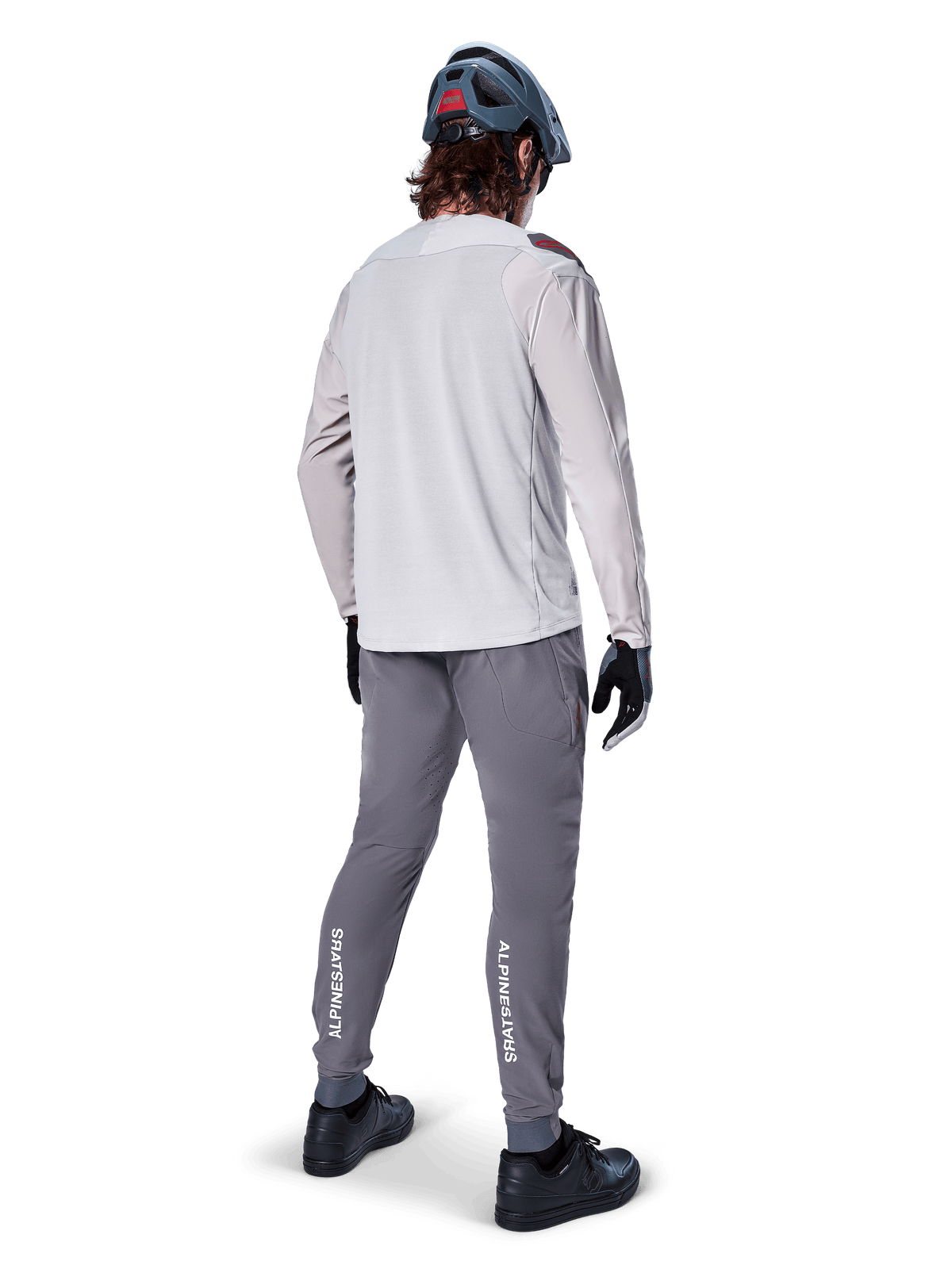 Pantalon Alpinestars A-Aria Elite, pantalon de cyclisme VTT, gris foncé, vue arrière d'un cycliste portant une tenue complète, logos Alpinestars blancs sur le bas des jambes, coupe performance avec perforations laser, associé à un maillot à manches longues gris clair et un casque de VTT gris