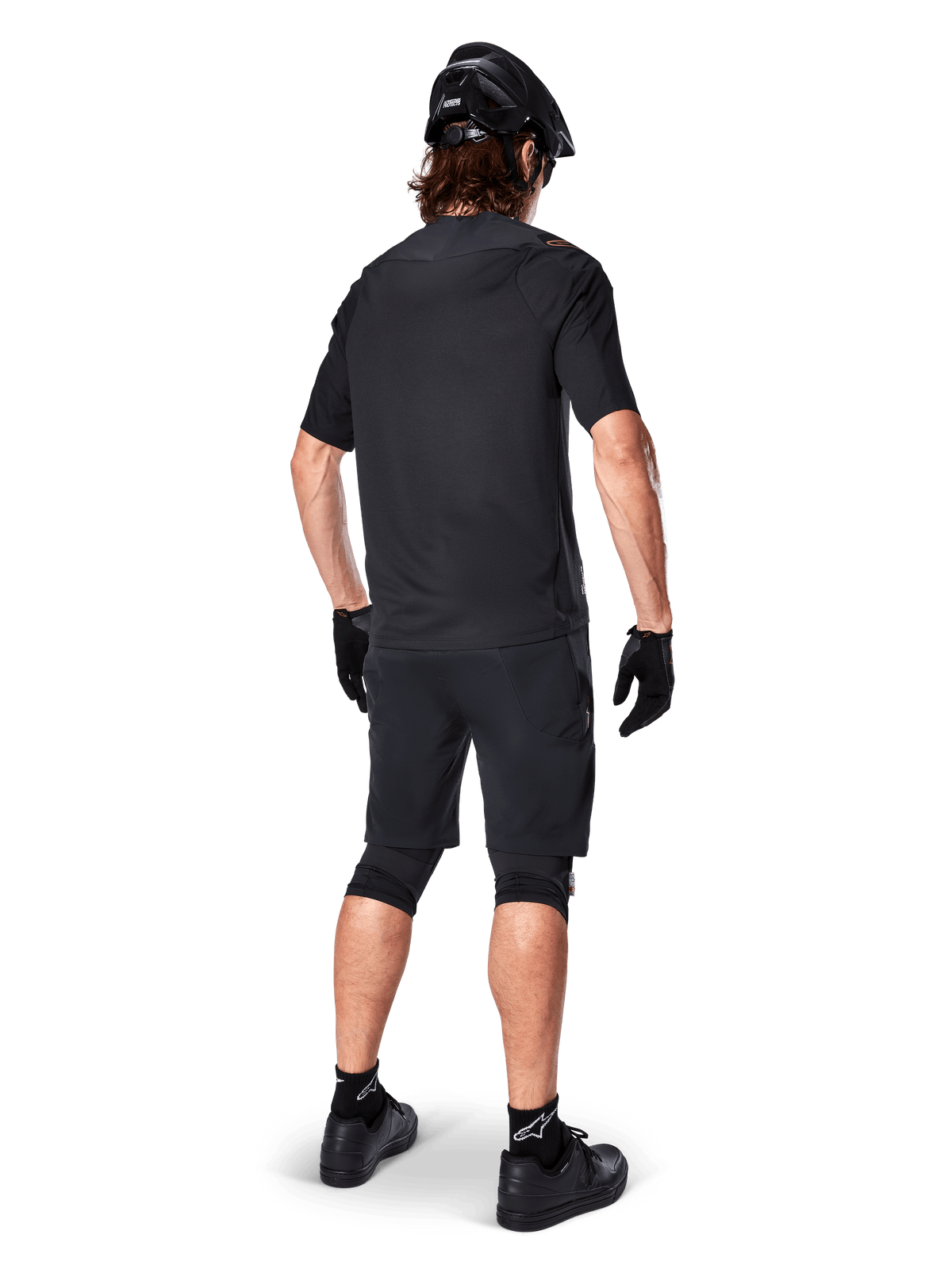 Achteraanzicht van een mountainbiker die Alpinestars A-Aria Elite Shorts in het zwart draagt, gecombineerd met een bijpassende zwarte jersey met korte mouwen, zwarte helm, handschoenen en MTB-schoenen, wat een complete performance-outfit voor off-road fietsen toont.