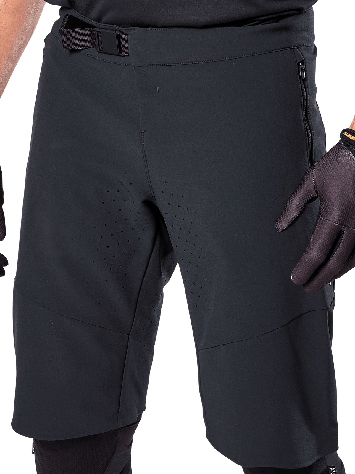 Alpinestars A-Aria Elite Shorts in zwart, close-up van de taille en dij, voorzien van magnetische gespsluiting, zakken met ritssluiting en lasergesneden ventilatieperforaties, gedragen met zwarte fietshandschoenen voor mountainbiken