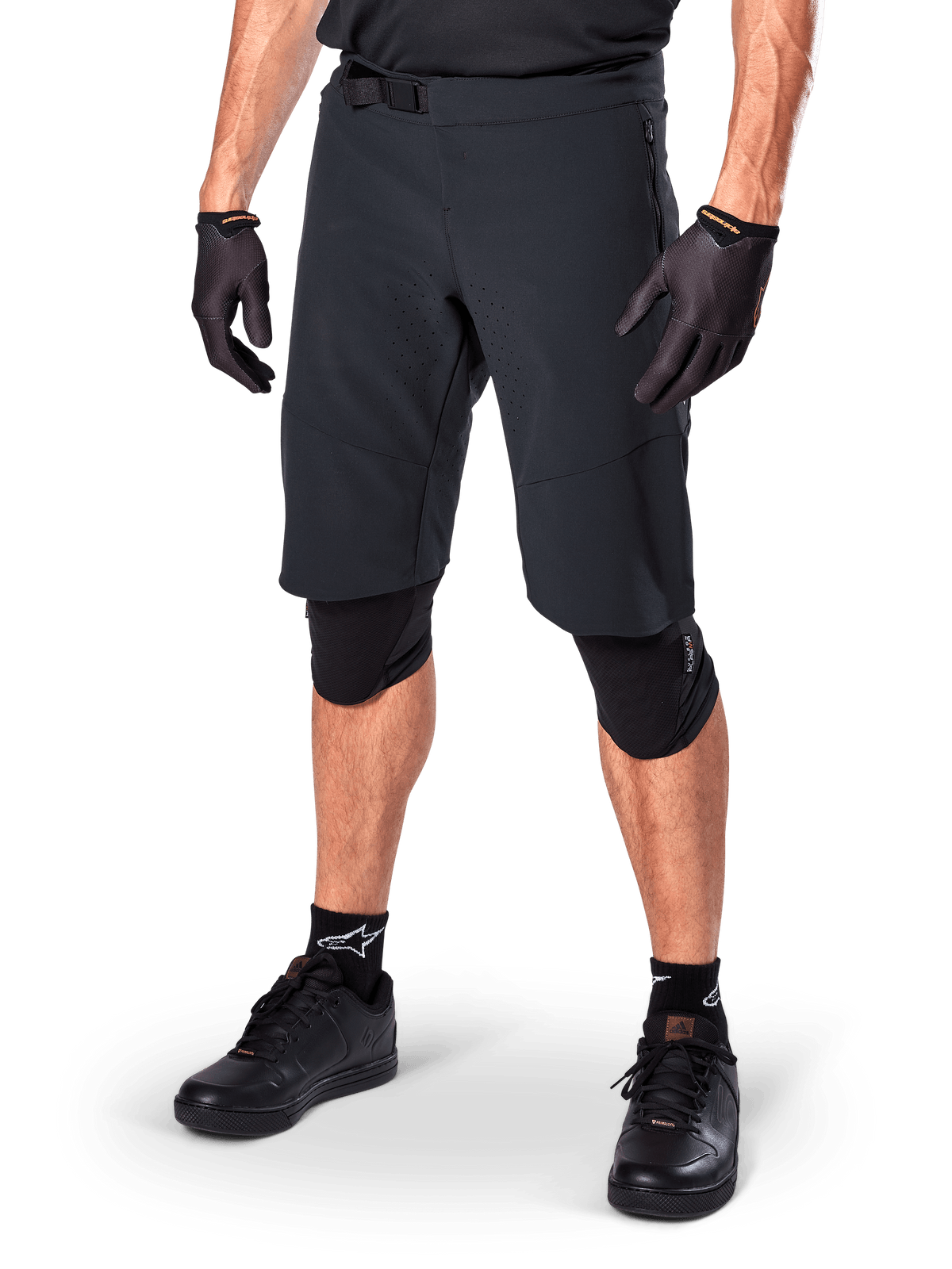 Alpinestars A-Aria Elite Shorts, zwarte mountainbike broek, gedragen met bijpassende zwarte handschoenen en kniebeschermers, voorzien van een magnetische gesp en lasergesneden perforaties, strak ontwerp voor off-road mountainbiken