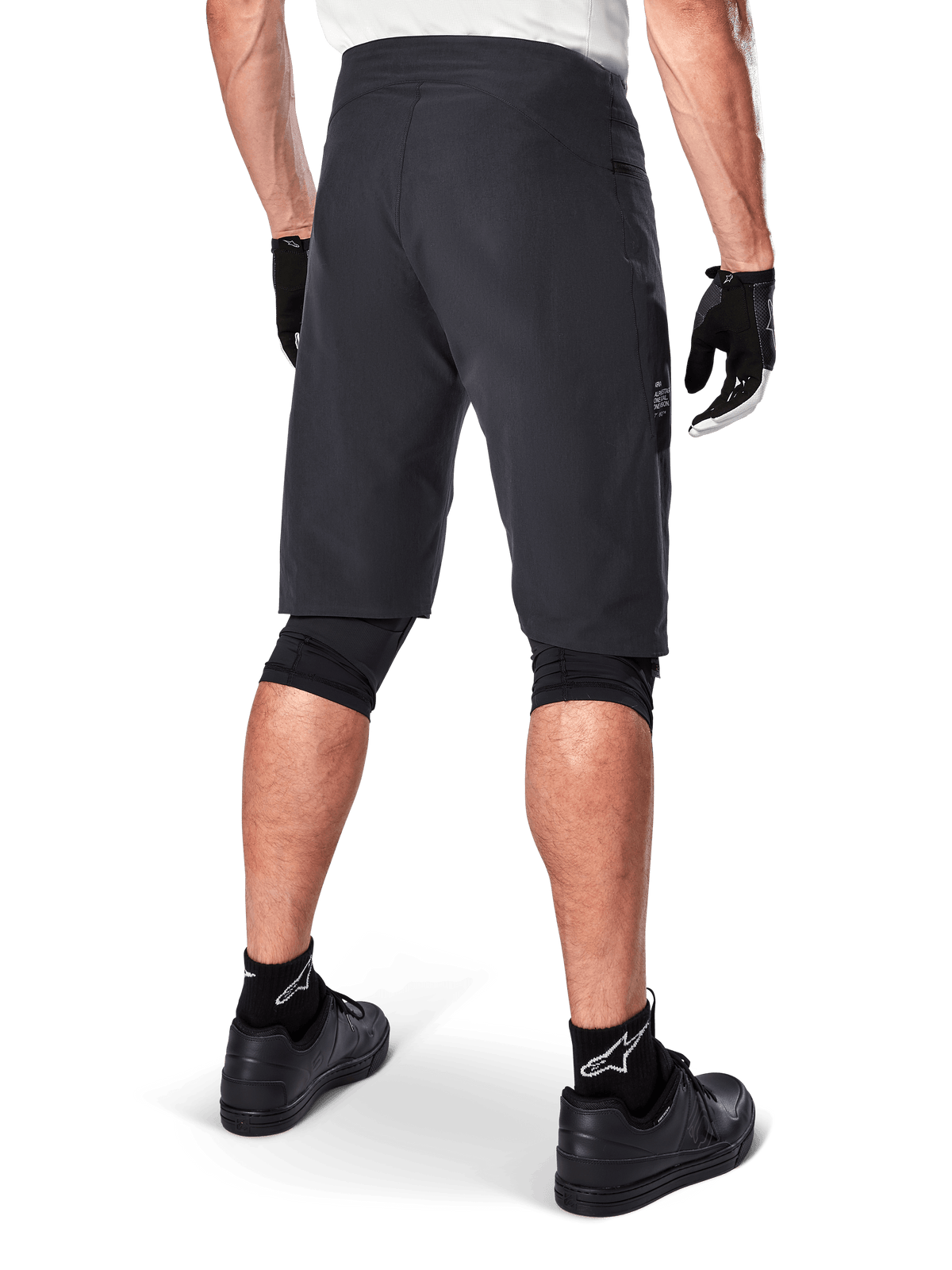Alpinestars A-Aria Shorts, mountainbike short, zwart, achteraanzicht met prestatiepasvorm en strak ontwerp, gedragen met zwarte handschoenen en sokken met het witte Astars-logo, technische wielerkleding voor off-road rijden