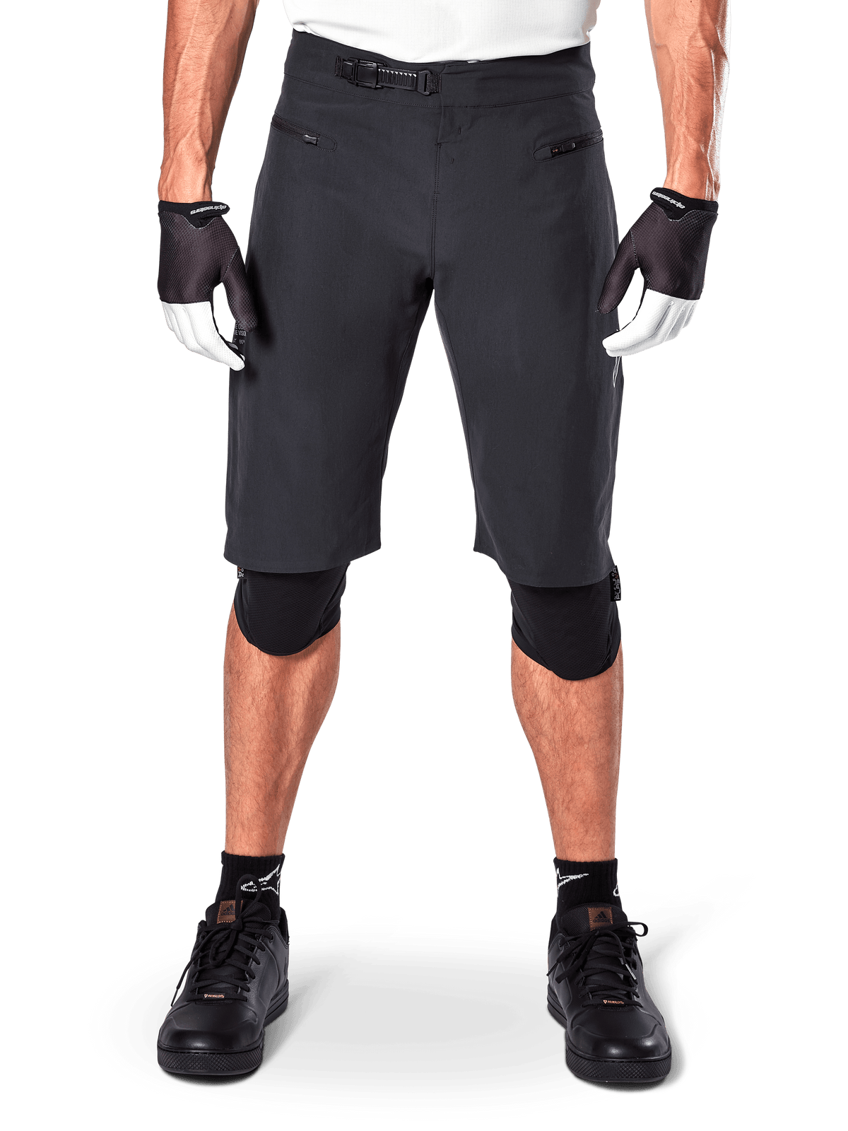 Alpinestars A-Aria Shorts, zwarte mountainbike shorts, voorzien van een ratelsluiting in de taille en ritszakken, gedragen met zwart-witte handschoenen en kniebeschermers, technische fietskleding voor off-road ritten