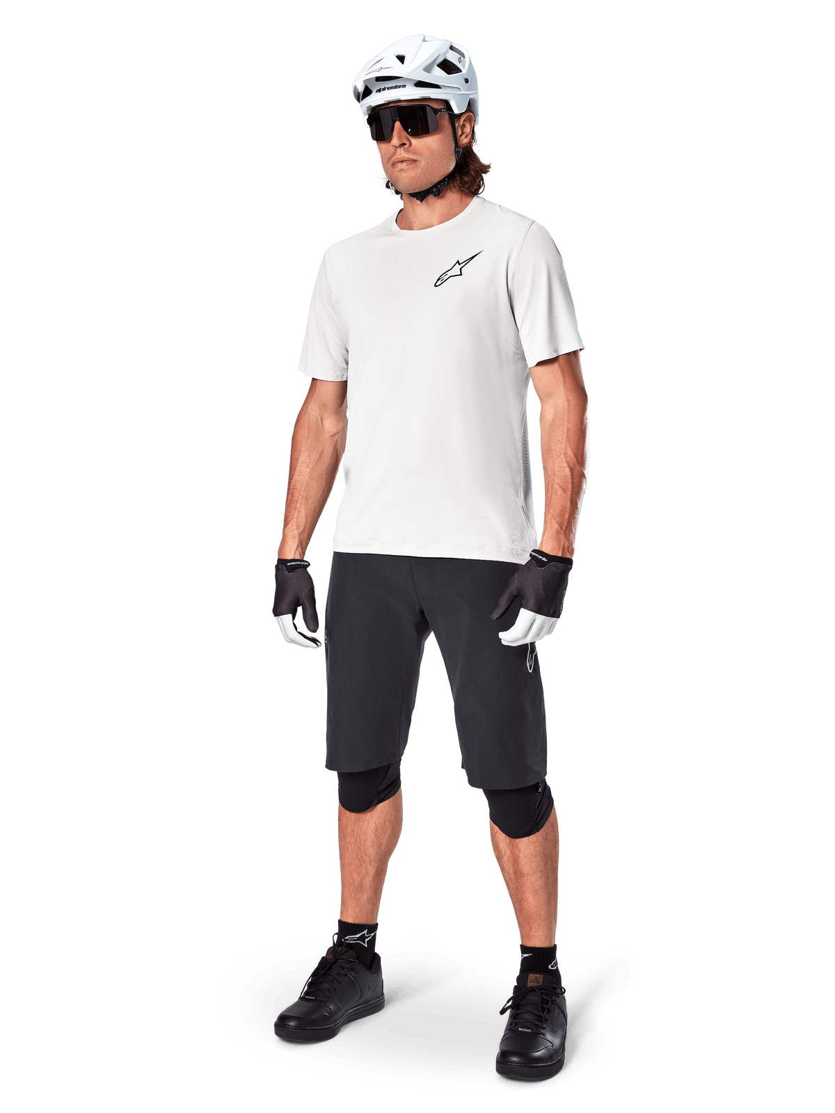 Mannelijke mountainbiker draagt Alpinestars A-Aria Shorts, zwarte fietsshort, gecombineerd met een witte jersey met korte mouwen, witte mountainbikehelm en zwarte performance gear, volledige outfit voor off-road trailrijden