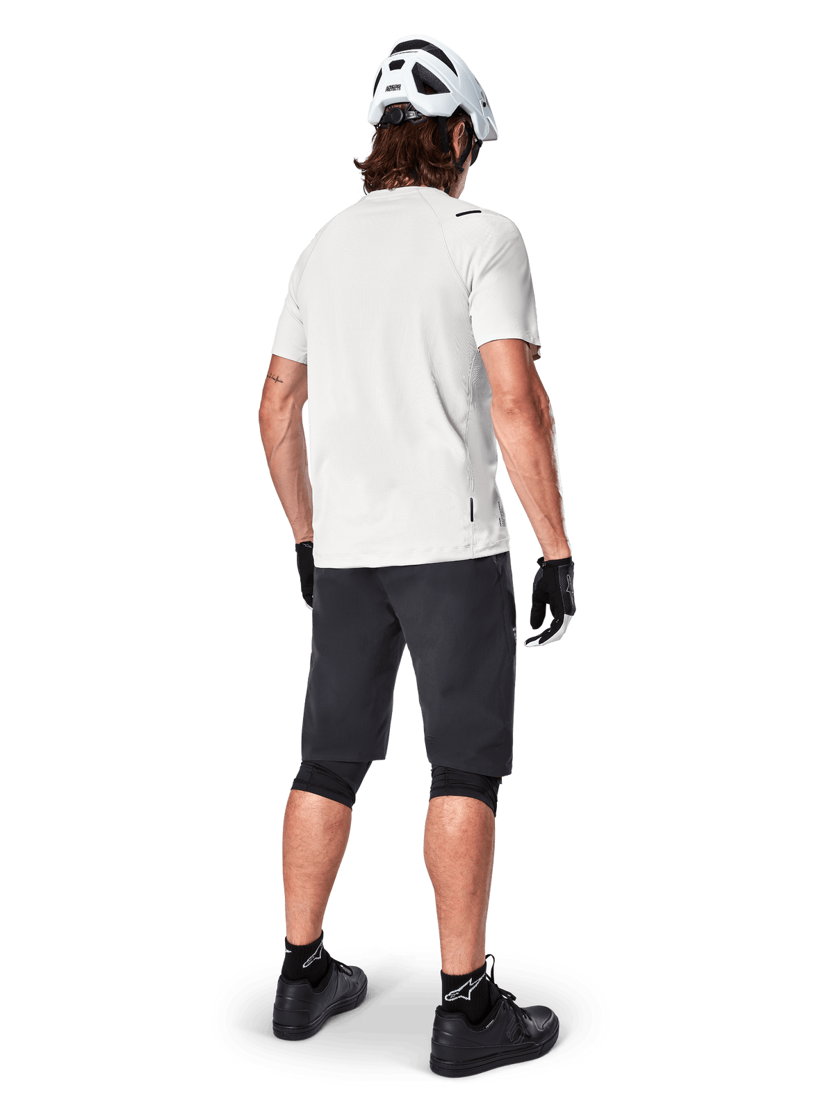 Mountainbiker van achteren gezien in Alpinestars A-Aria Shorts in het zwart, wit performance shirt met korte mouwen, witte helm, zwarte handschoenen en zwarte mountainbikeschoenen, fietskleding voor trailrijden