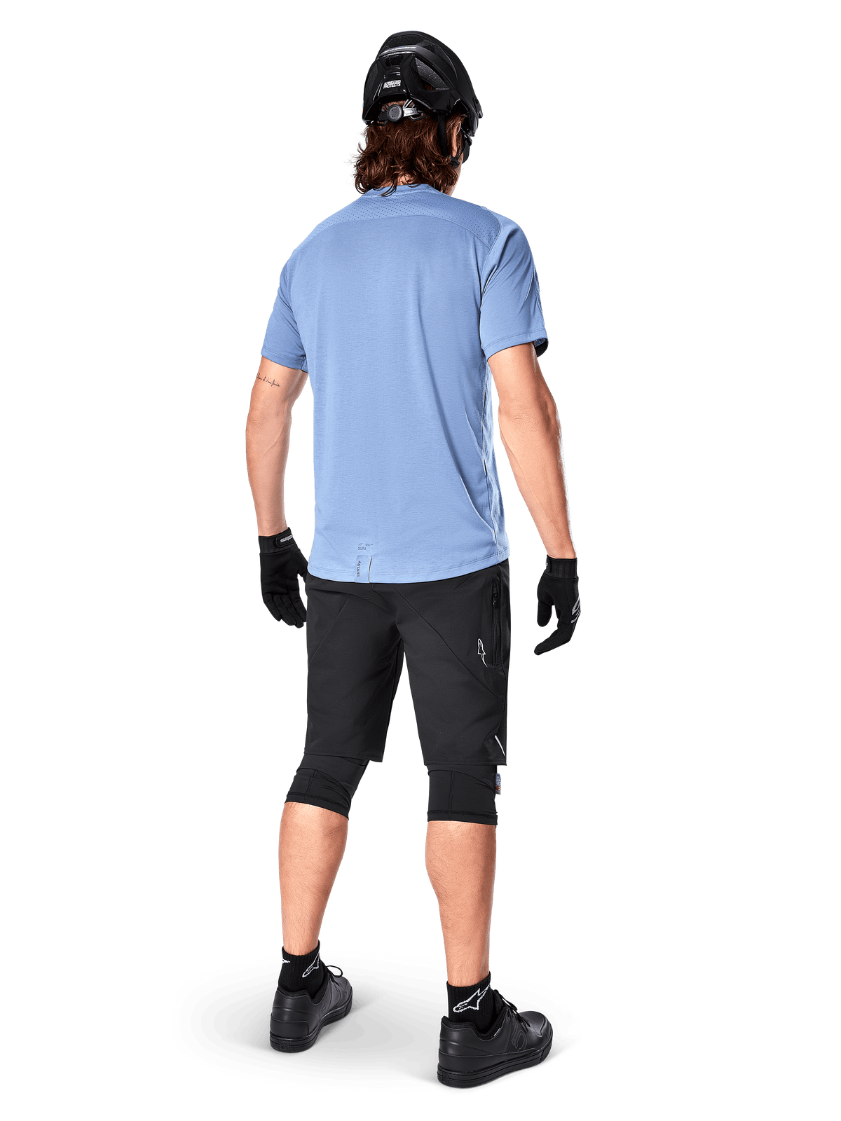Alpinestars A-Dura Elite Shorts, Mountain Bike Shorts, Black, rear view on model, worn with light blue short-sleeve shirt and black protective gear, technical design with zippered pockets and reflective details for off-road cycling
