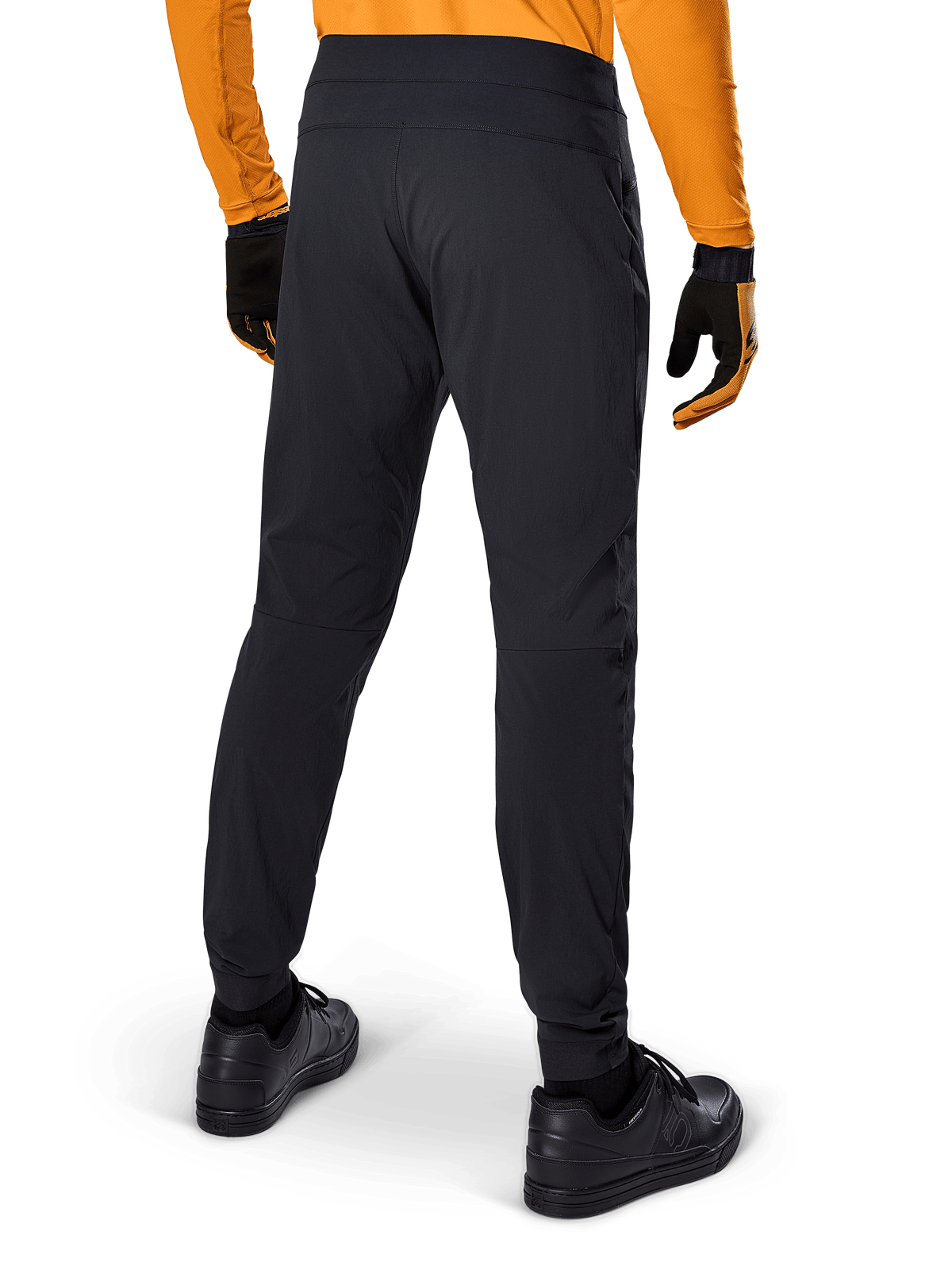 Alpinestars A-Dura Pants, zwarte MTB-broek, achteraanzicht, gedragen met een oranje jersey met lange mouwen en zwarte handschoenen, voorzien van elastische manchetten en duurzaam textielmateriaal voor mountainbiken