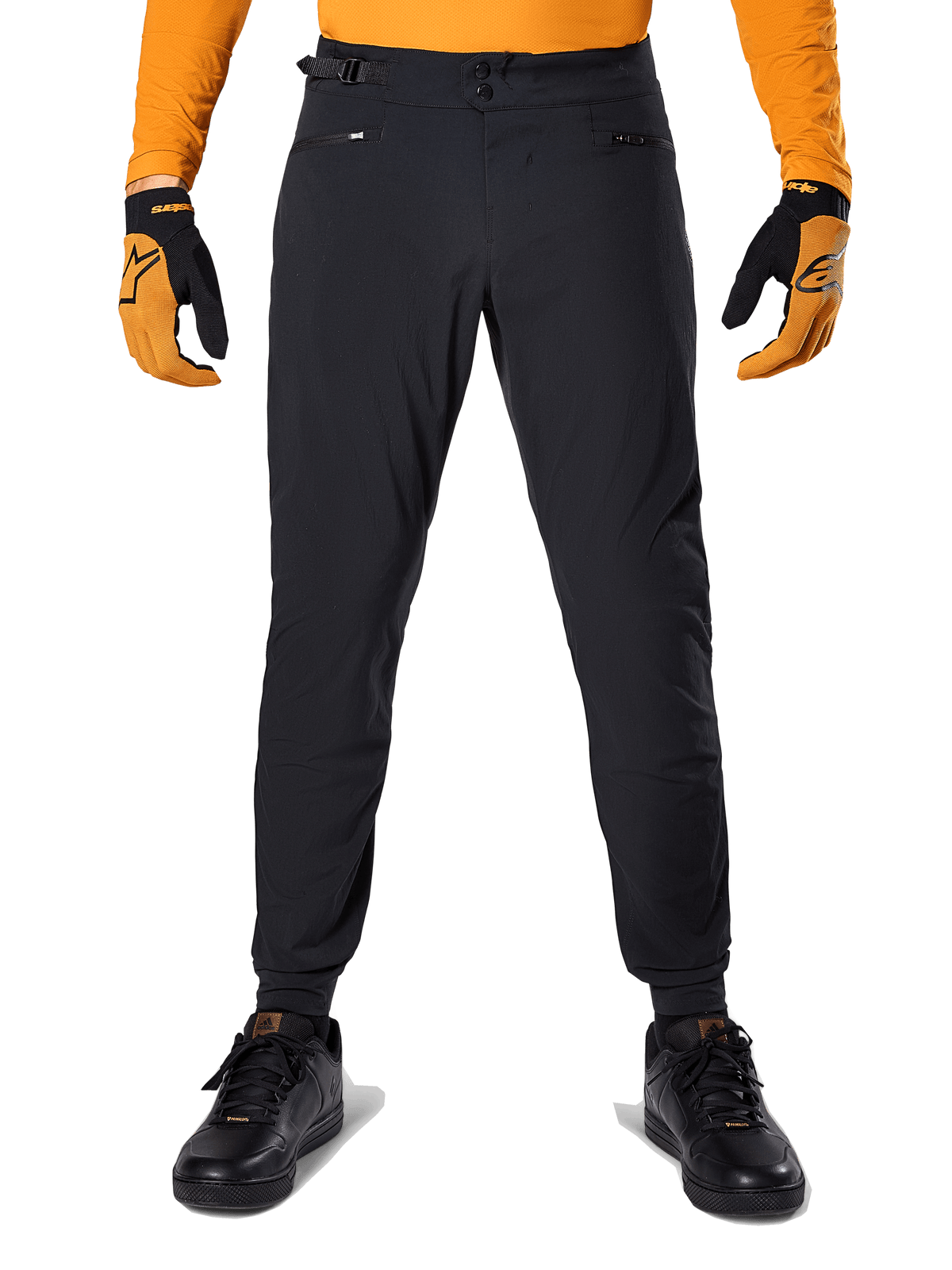 Alpinestars A-Dura broek, mountainbikebroek, zwart, gedragen met een oranje jersey met lange mouwen en zwart-oranje handschoenen, met een dubbele drukknoopsluiting en verstelbare tailleband aan de zijkant, duurzaam textiel voor mountainbiken