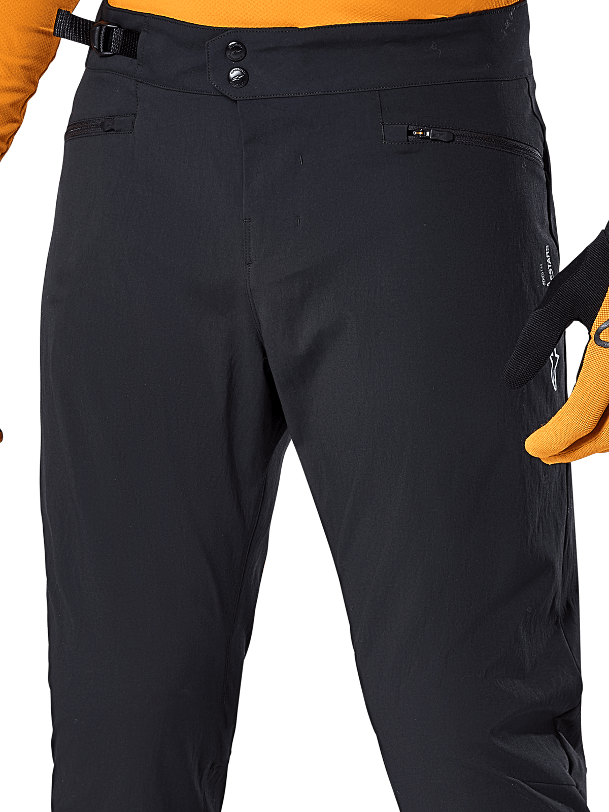 Alpinestars A-Dura Pants, zwarte MTB-broek, close-up met dubbele drukknoopsluiting, verstelbare tailleband aan de zijkant en zakken met rits, gecombineerd met een oranje jersey en handschoenen