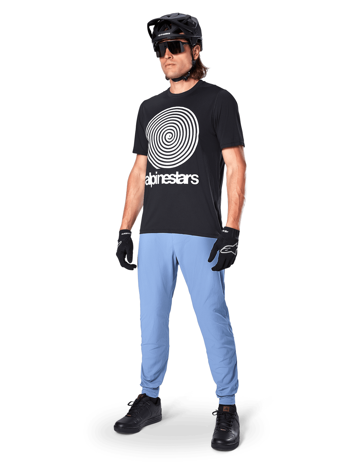 Alpinestars A-Dura broek, MTB-broek, Infinity Blue, gedragen met zwart grafisch T-shirt met wit spiraallogo, zwarte helm, zonnebril en zwarte handschoenen, professionele mountainbike-uitrusting