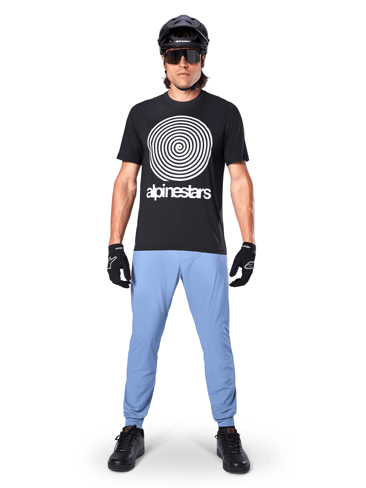 Alpinestars A-Dura broek, Infinity Blue, MTB-broek gedragen met een zwart t-shirt met spiraalvormige print, zwarte handschoenen en een zwarte helm, voorzien van duurzame stretchstof en elastische manchetten, hoogwaardige mountainbike-uitrusting