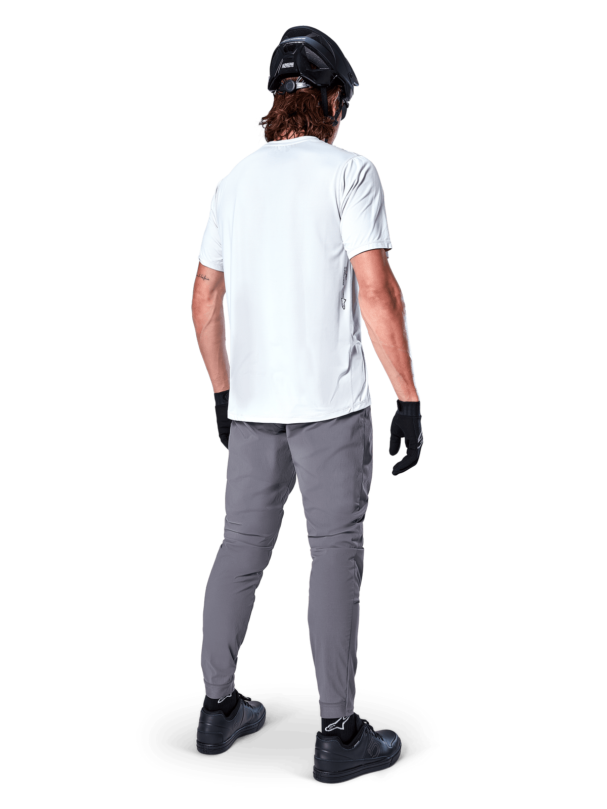 Alpinestars A-Dura Pants, Dark Gray Mountain Bike Pants shown from the back, worn with a white short-sleeve t-shirt, black MTB helmet, black gloves and shoes, regular fit design with elasticated cuffs, durable off-road cycling gear