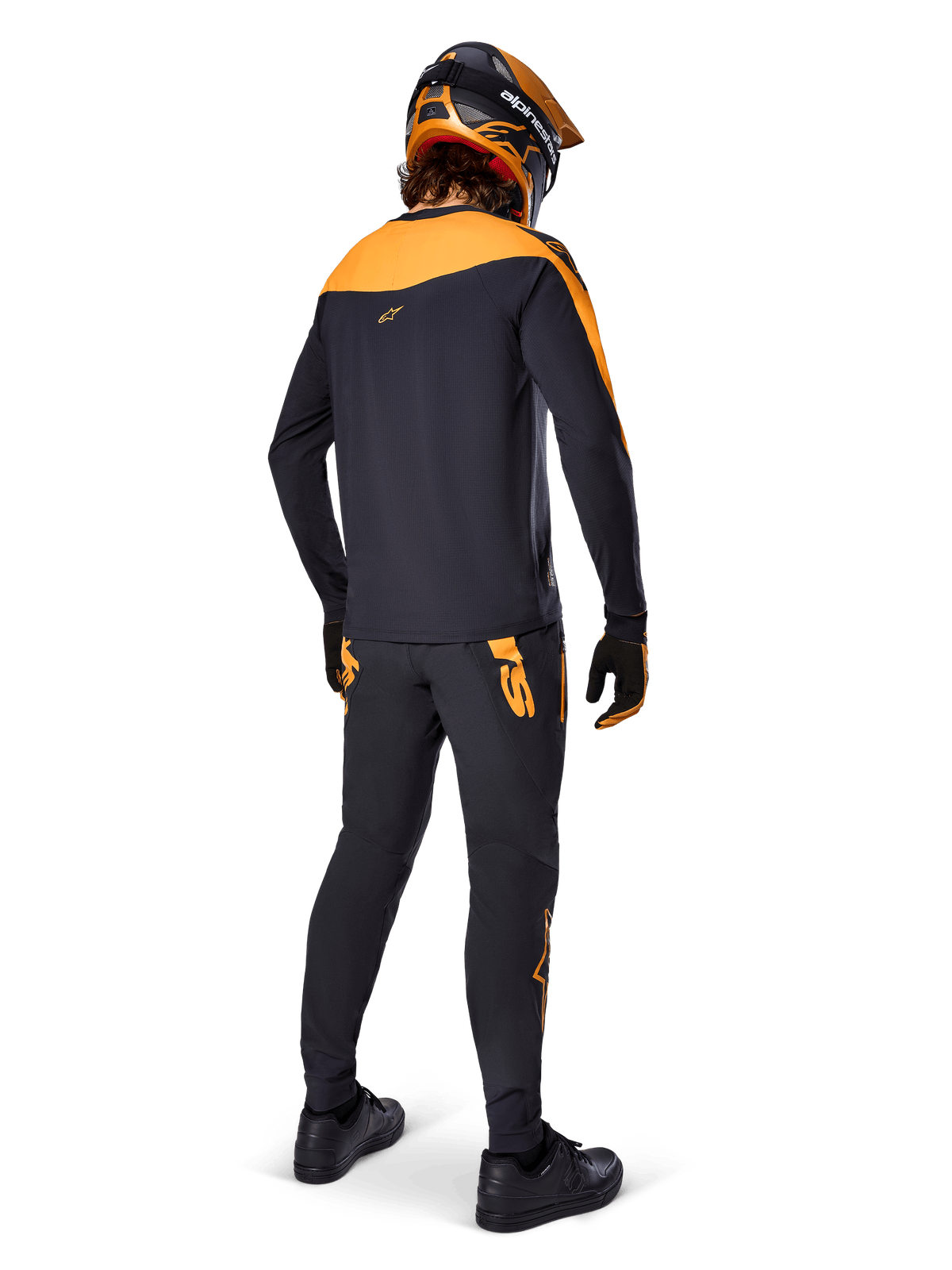 Alpinestars A-Supra Race Pants, MTB Racing Pants, Black with orange logos, viewed from the back on a rider wearing a matching black and orange jersey, helmet, and gloves, highlighting the MX-inspired wordmark on the back yoke and performance fit for technical trails.