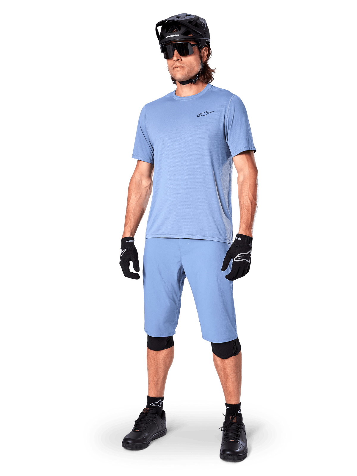Modèle portant le short Alpinestars A-Dura en Infinity Blue, maillot à manches courtes bleu clair assorti, casque de VTT noir, lunettes de soleil et gants noirs, tenue de VTT complète pour le trail