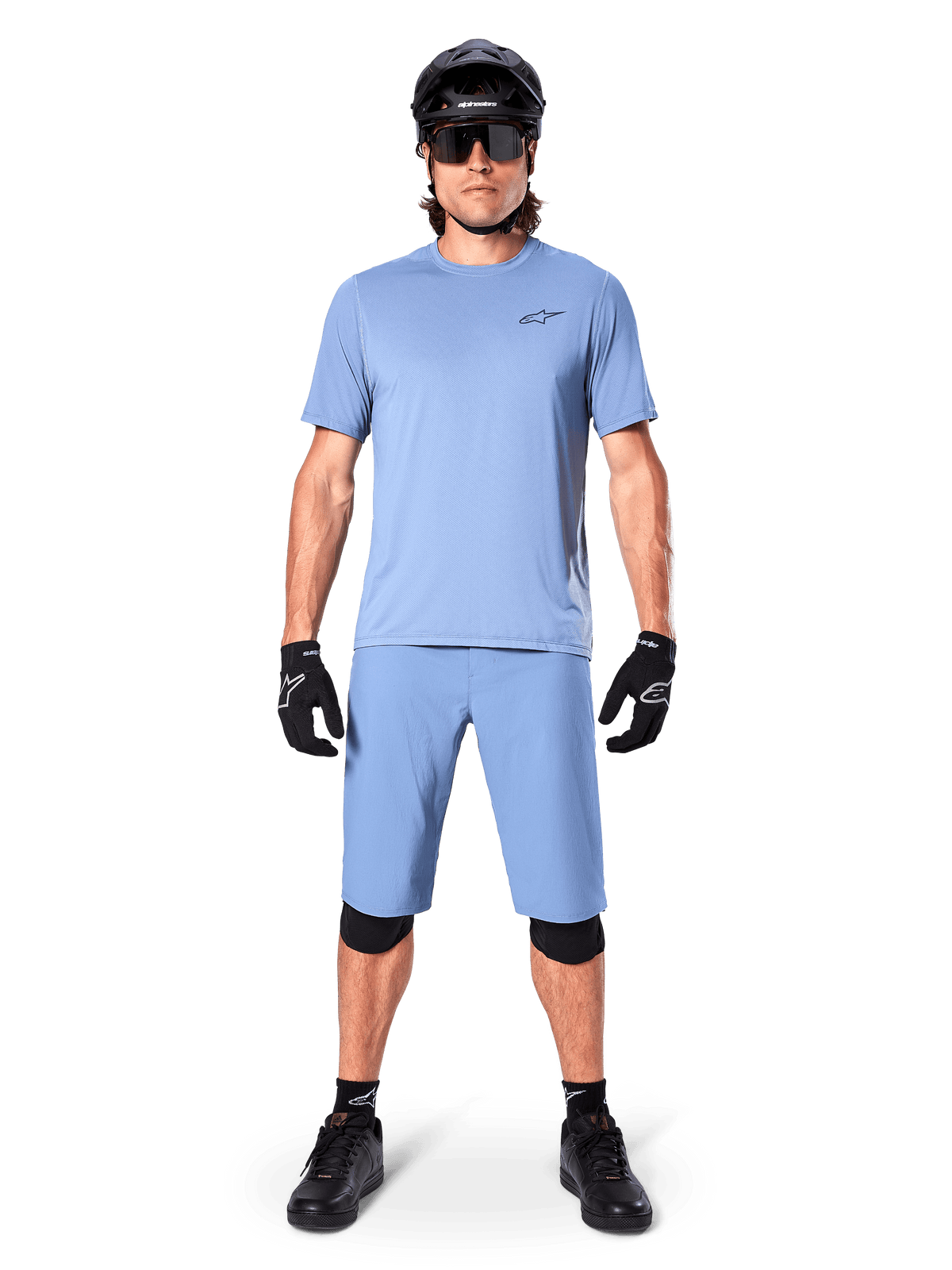 Modèle portant le short Alpinestars A-Dura en Infinity Blue, maillot bleu clair assorti, casque de VTT noir, lunettes de soleil noires, gants et genouillères noirs, tenue de VTT complète pour le trail