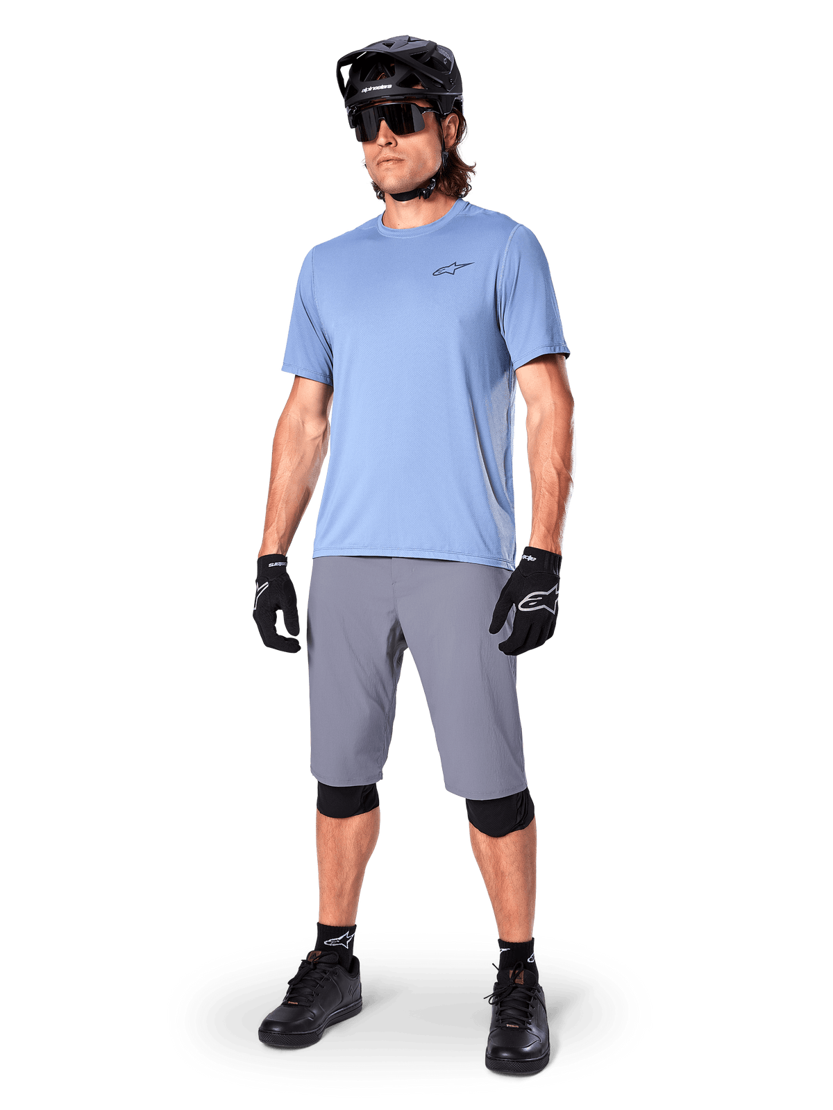 Alpinestars A-Dura Shorts, MTB-short, donkergrijs, gedragen door een rijder met een lichtblauwe jersey, zwarte MTB-helm, zwarte handschoenen en kniebeschermers, complete mountainbike-outfit voor trail- en offroad-ritten