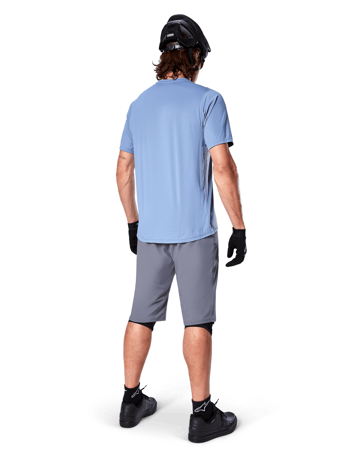 Alpinestars A-Dura Shorts, donkergrijze MTB-shorts, achteraanzicht, gedragen met een lichtblauwe jersey met korte mouwen en zwarte mountainbikehelm, zwarte handschoenen en sokken met zwarte schoenen, functionele en duurzame uitrusting voor off-road fietsen