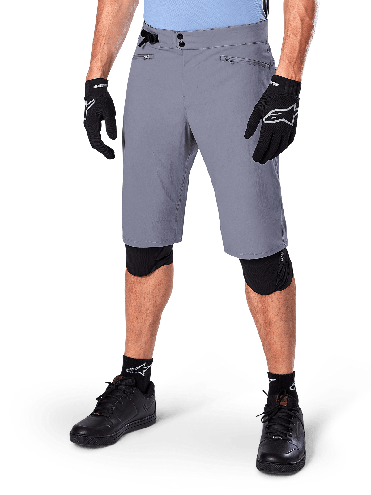 Alpinestars A-Dura Shorts, donkergrijze mountainbike shorts, gecombineerd met zwarte handschoenen en kniebeschermers, voorzien van zakken met ritssluiting en een dubbele drukknoopsluiting, robuuste fietskleding voor off-road trails