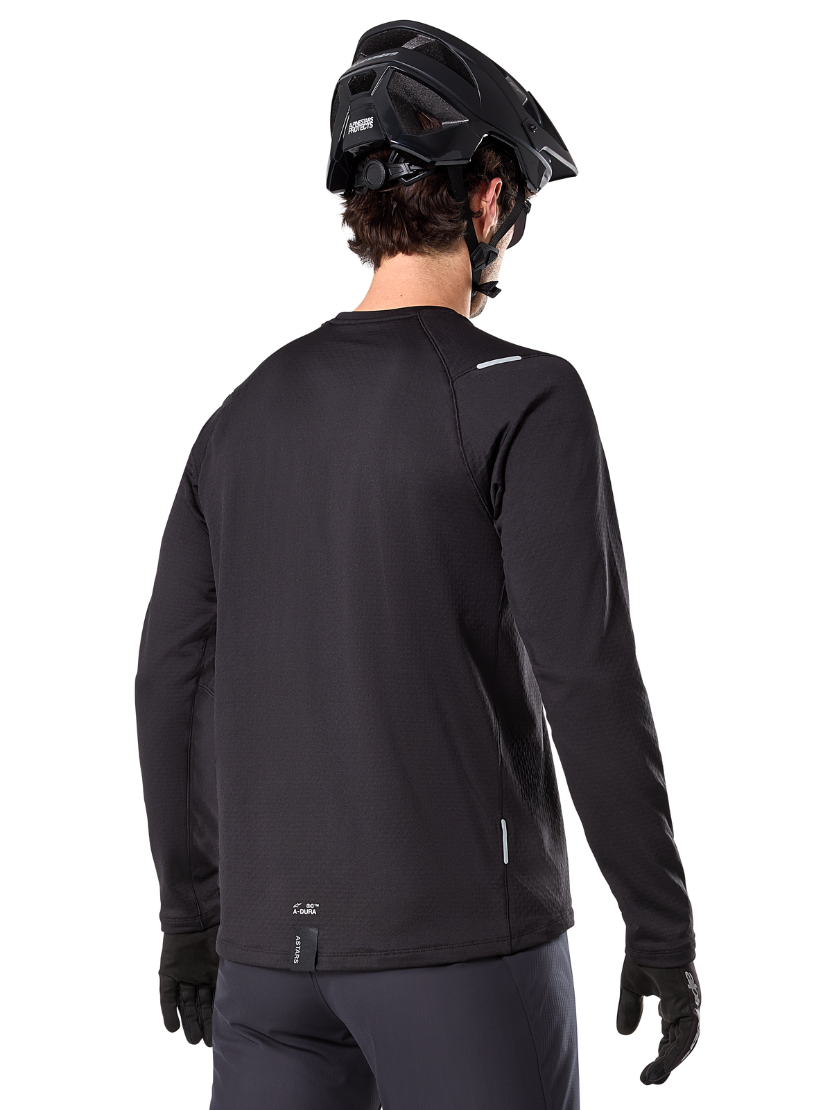 Alpinestars A-Dura Thermal Jersey, mountainbike jersey met lange mouwen, zwart, achteraanzicht met verlengde achterkant, kleine reflecterende details en branding op de zoom, gedragen met een zwarte helm en handschoenen voor fietsen in koud weer
