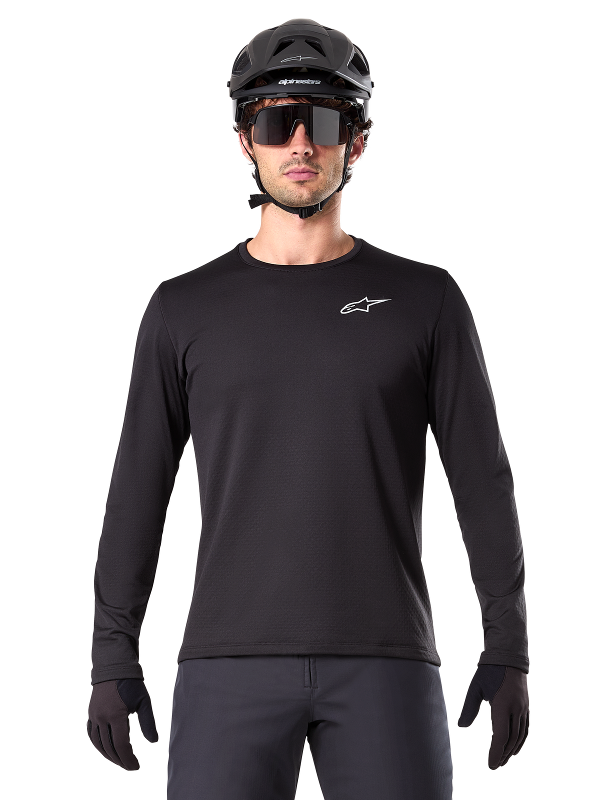 Alpinestars A-Dura Thermal Jersey, zwart mountainbike jersey met lange mouwen, gedragen met een zwarte helm en grote zonnebril, voorzien van een klein wit Alpinestars-logo op de borst, normale pasvorm, MTB-fietskleding