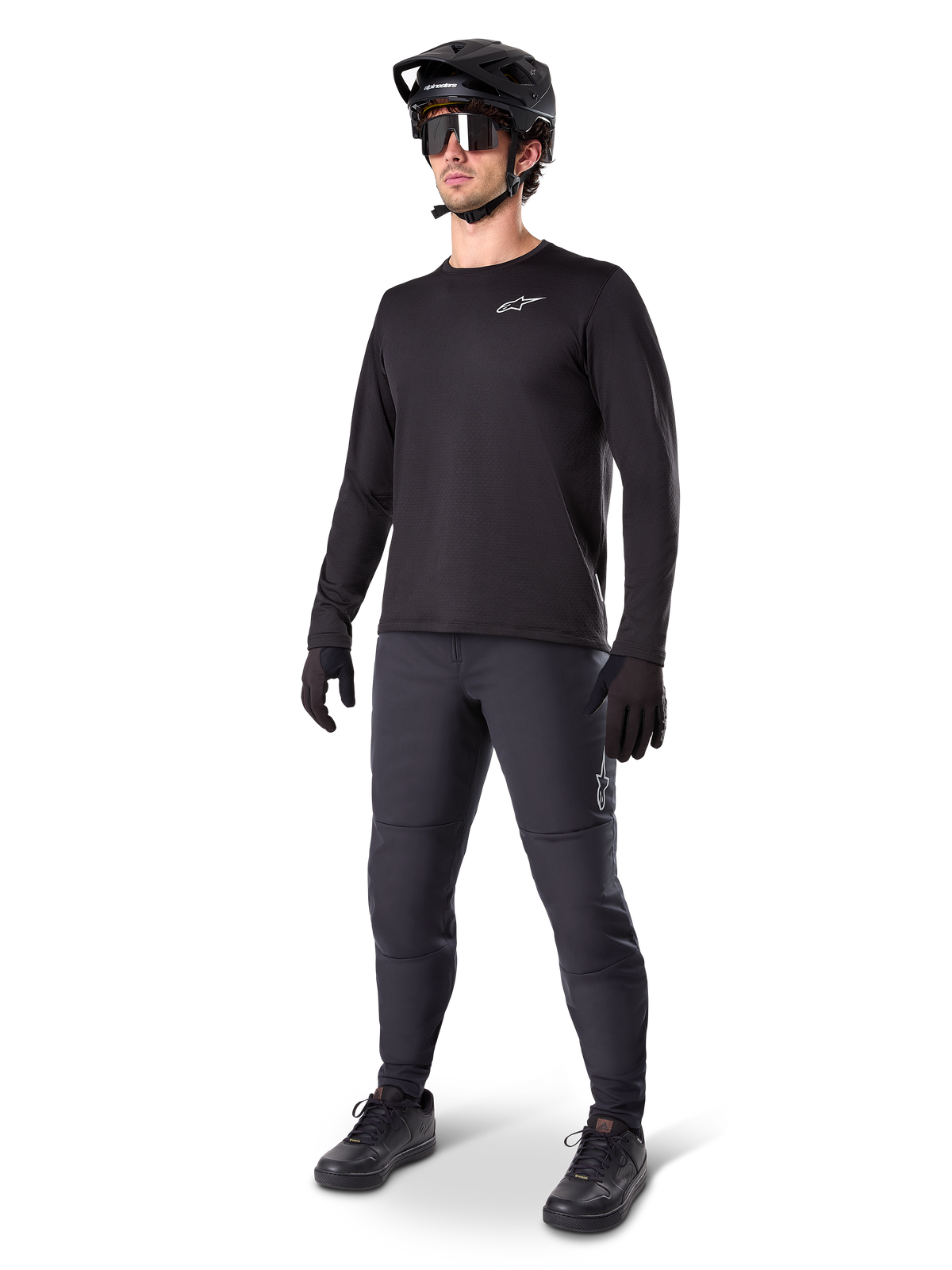Model draagt Alpinestars A-Dura Thermal Jersey, zwart MTB-shirt met lange mouwen, zwarte mountainbikehelm, zonnebril en donkergrijze broek, voorzien van een klein wit logo op de borst, geïsoleerde fleececonstructie voor ritten in koud weer