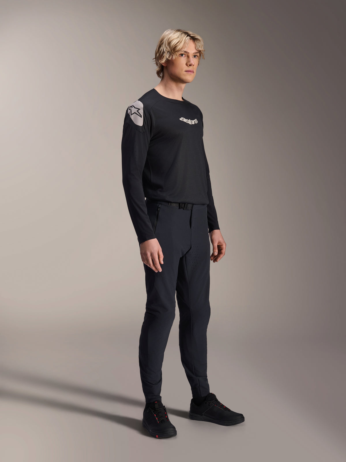 Männliches Model in Alpinestars A-Aria Elite Hose in Black Titanium und Aria Polartec Elite LS Trikot, schwarze Mountainbike-Performance-Ausrüstung, mit laserperforierter Belüftung und Magnetverschluss an der Hose, langärmeliges Trikot mit weißen Logos, komplettes Offroad-Cycling-Outfit