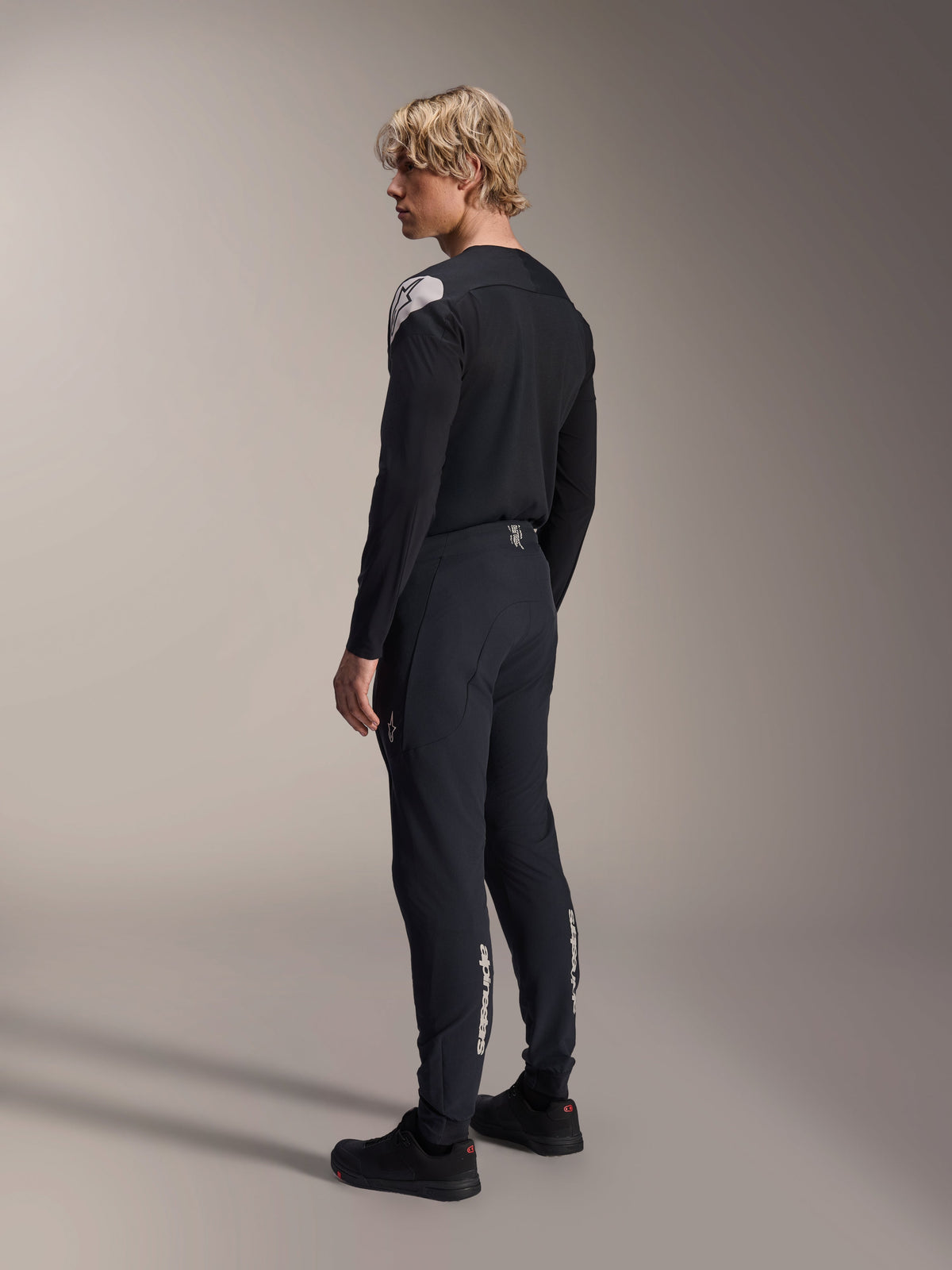 Alpinestars A-Aria Polartec Elite Langarm-Trikot, Schwarz, getragen von einem Modell in der Rückansicht im Profil, mit weißem Logo auf der Schulter, kombiniert mit einer passenden schwarzen Radhose für ein professionelles MTB-Outfit.
