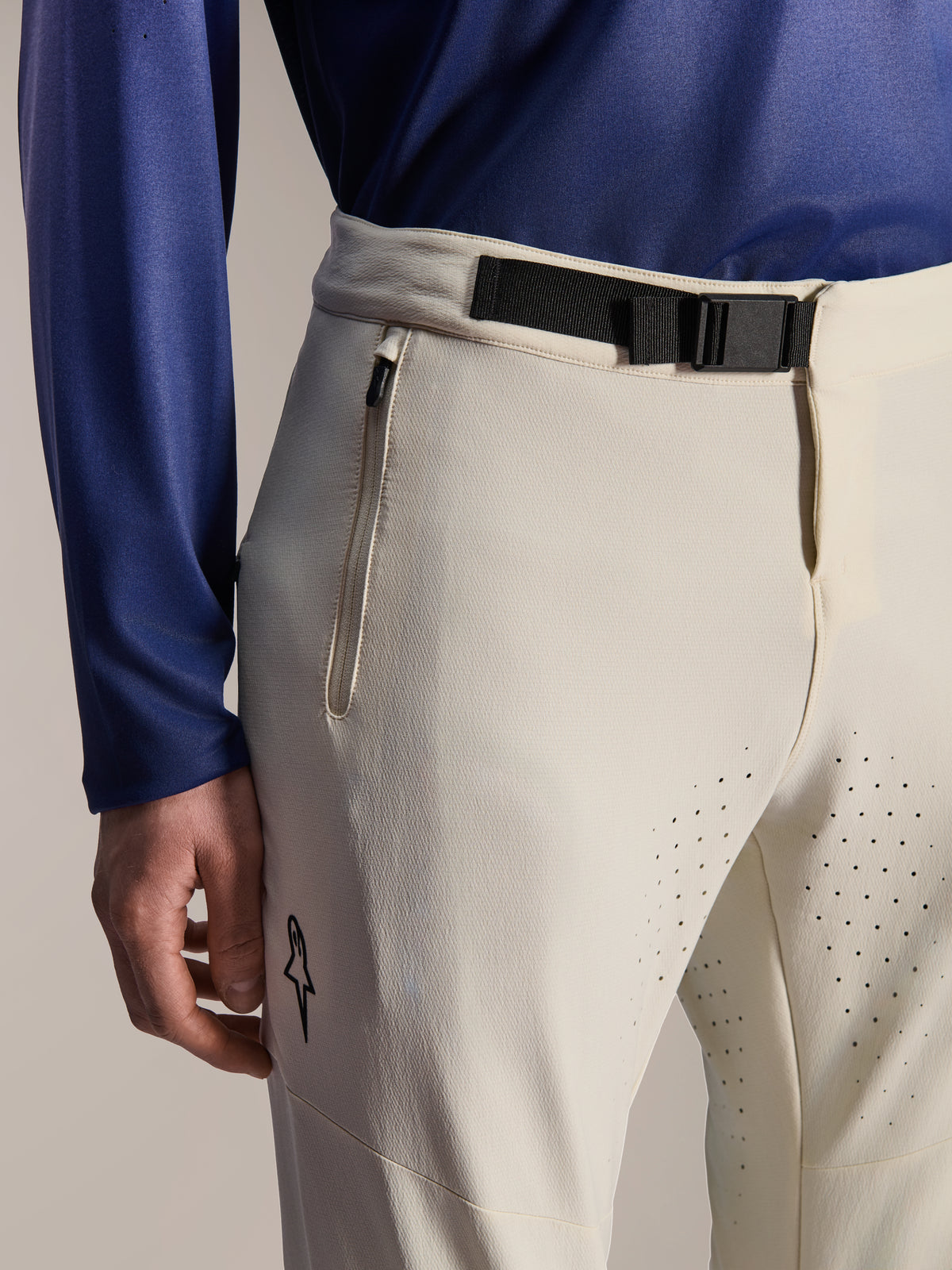 Alpinestars A-Aria Elite broek, mountainbikebroek, ecru, close-up van een zwarte magnetische gespsluiting in de taille, zak met rits en lasergesneden ventilatiegaten, hoogwaardige off-road fietskleding