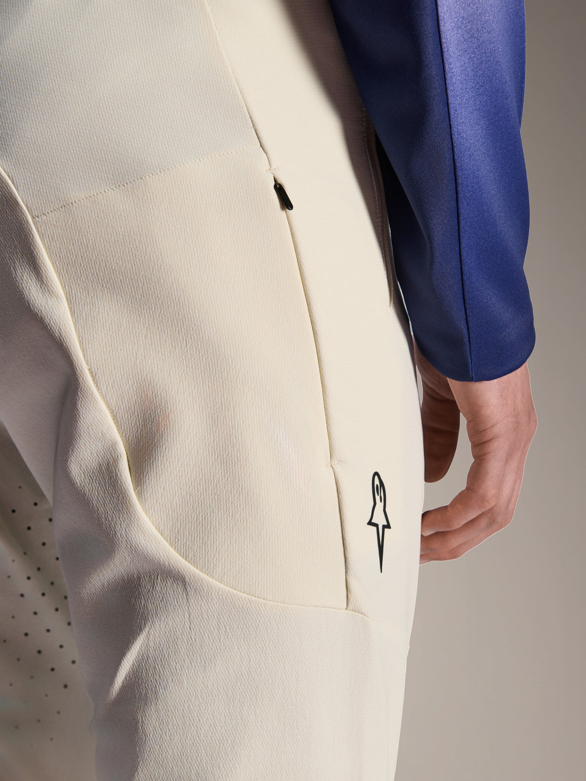 Alpinestars A-Aria Elite broek, ecru gebroken witte performance broek, close-up van zijzak met rits en laserperforaties voor ventilatie, minimalistisch logodetail, high-stretch stof voor mountainbiken