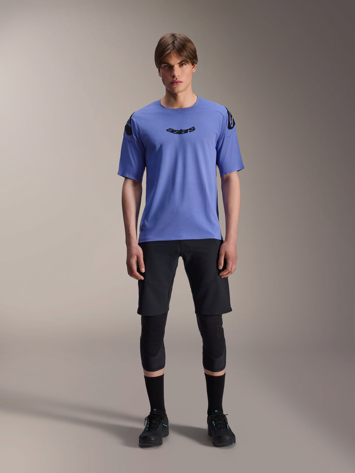 Alpinestars A-Aria Elite Shorts, MTB mountainbike shorts, Black Titanium, gedragen met blauwe jersey met korte mouwen, kniebeschermers en zwarte fietsschoenen, full-body studio-opname, hoogwaardige mountainbikekleding