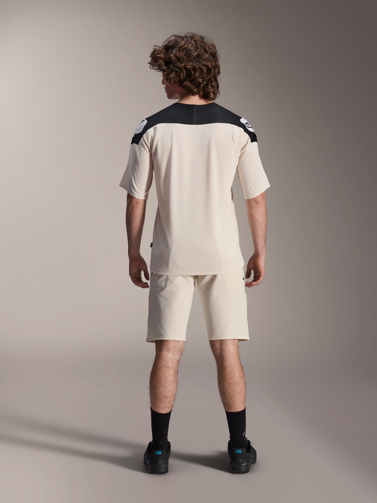 Alpinestars A-Aria Polartec Elite Jersey met korte mouwen, MTB-fietsshirt, ecru met zwarte schouderpanelen, achteraanzicht getoond met bijpassende short en zwarte sokken, prestatiegerichte pasvorm met een verlengde achterkant voor off-road rijden.