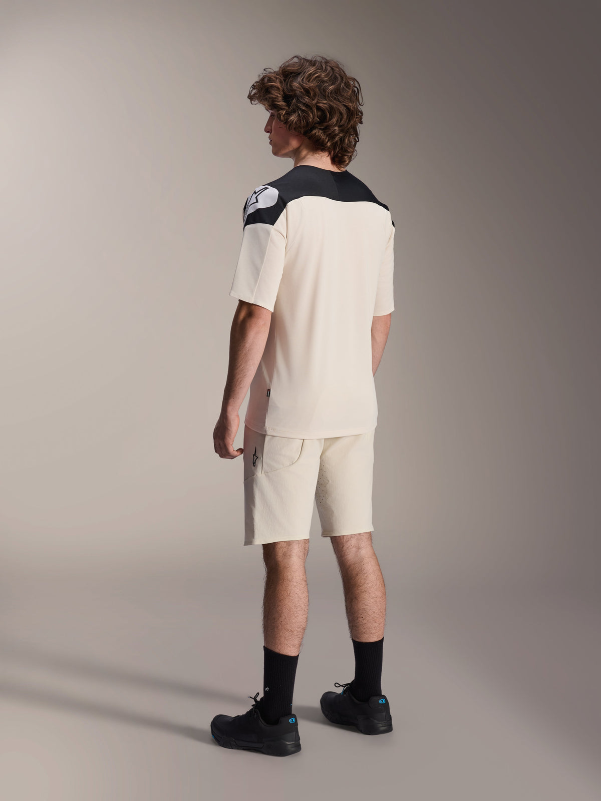 Alpinestars A-Aria Polartec Elite Jersey met korte mouwen in de kleur Ecru, van achteren gezien, voorzien van zwarte schouderpanelen met een wit logo, gecombineerd met een bijpassende ecru mountainbike short en zwarte schoenen