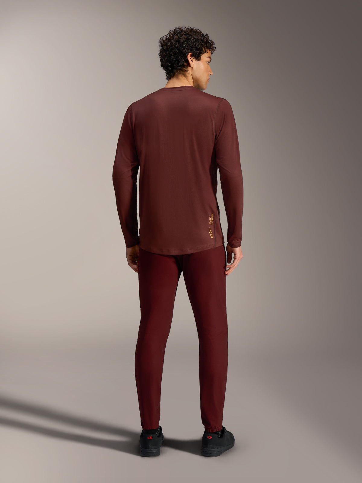 Bordeauxrotes A-Dura Ride Langarm-Trikot in der Rückansicht mit gelbem Alpinestars-Logo am unteren Rücken.