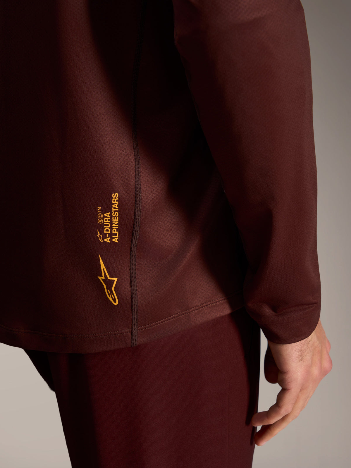 A-Dura Ride Langarmtrikot in Bordeaux, mit gelbem Alpinestars-Branding auf strukturiertem Funktionsgewebe.