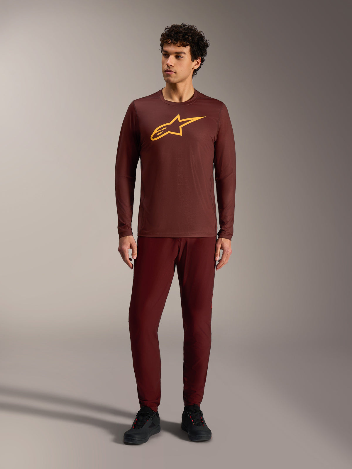 A-Dura Ride Langarmtrikot in Bordeaux mit gelbem Alpinestars-Logo und passender Hose für MTB-Trailfahrten.