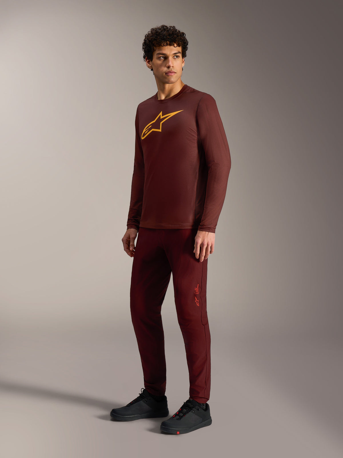 Bordeauxfarbenes A-Dura Ride Langarmtrikot mit gelbem Astars-Logo, passender Hose und schwarzen MTB-Schuhen.