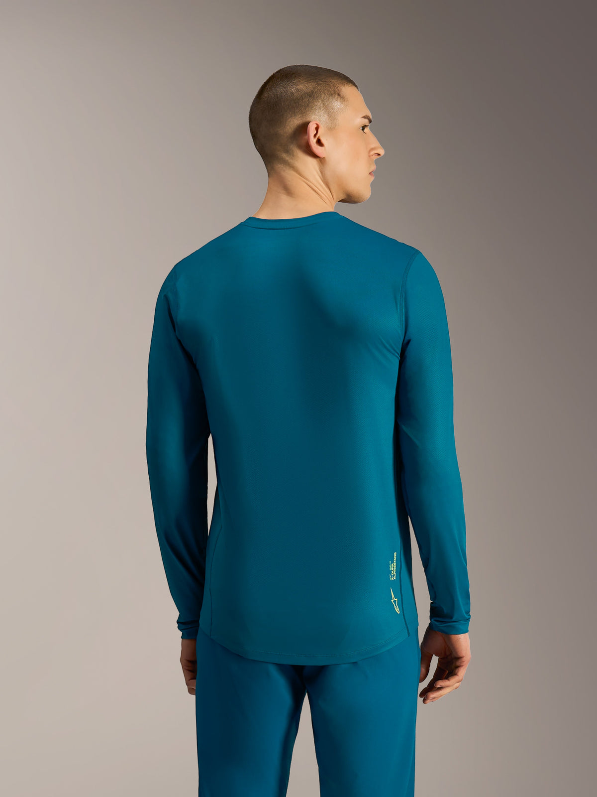 Blauwgroene A-Dura Ride jersey met lange mouwen, verlengde achterkant en Alpinestars-logo voor MTB-prestaties.