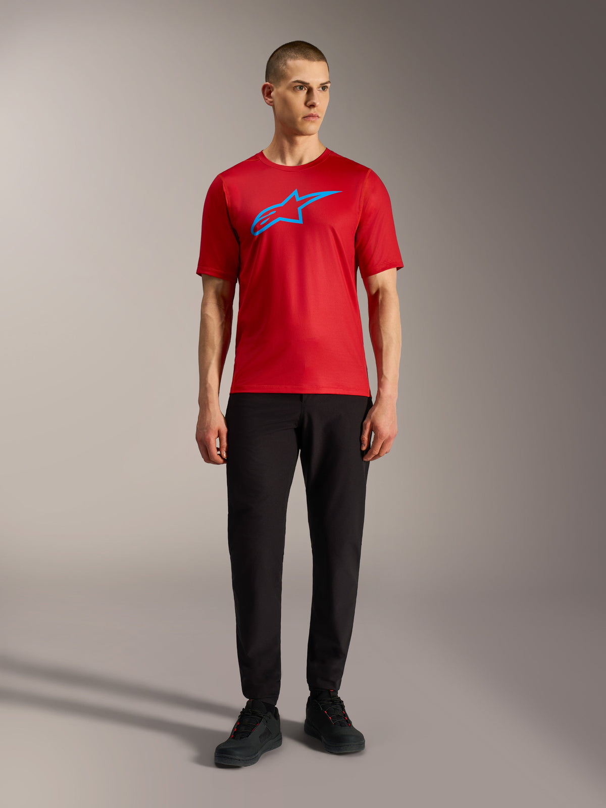 Rode Alpinestars A-Dura Ride trui met korte mouwen en blauw logo, gedragen met een zwarte broek voor een casual MTB-look.