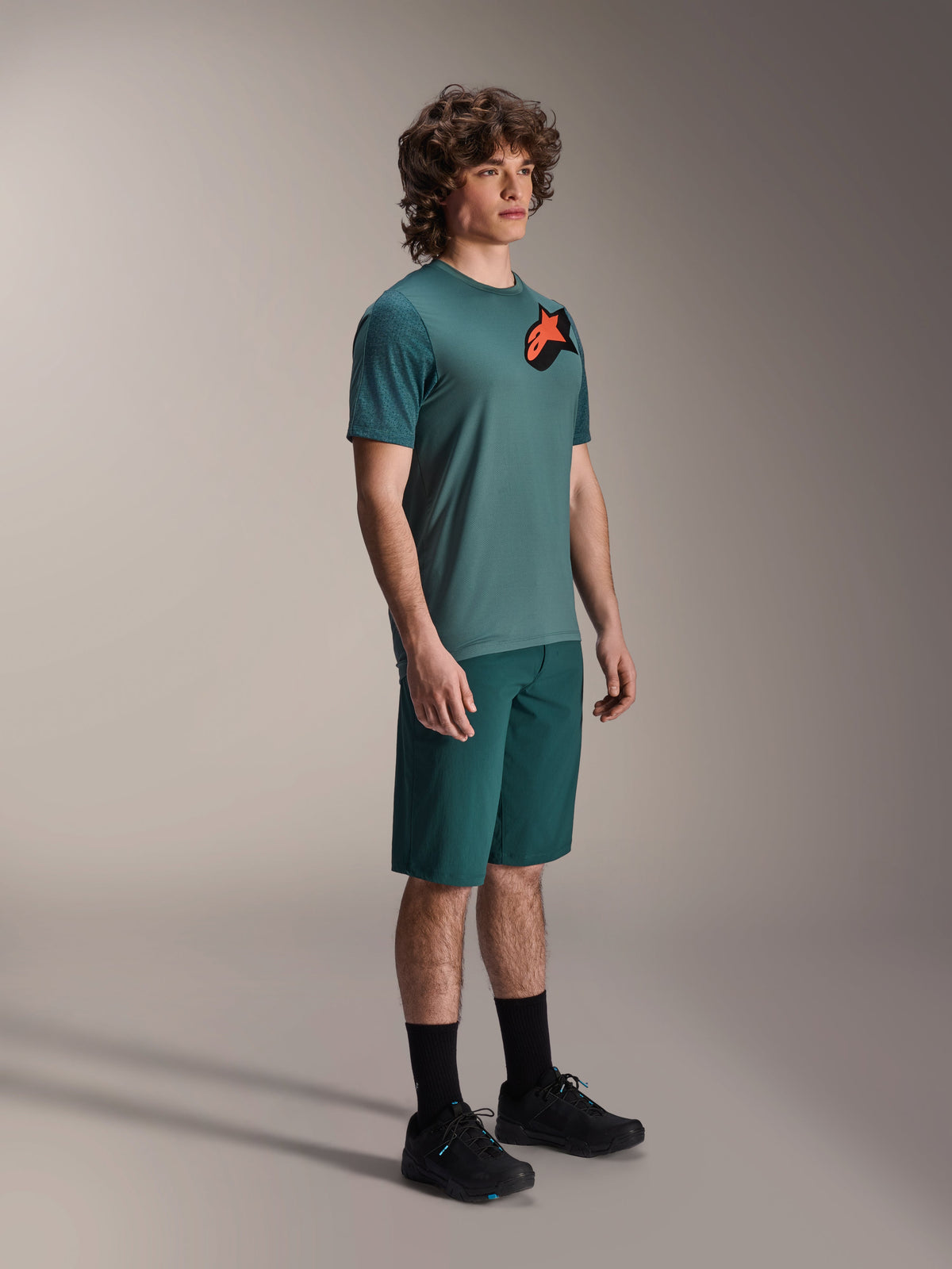 Maillot Alpinestars A-Dura Lipan, maillot de VTT à manches courtes, vert Silver Pine, avec un logo Astars orange et noir sur la poitrine, porté avec un short vert assorti et des chaussures de cyclisme noires, style trail décontracté