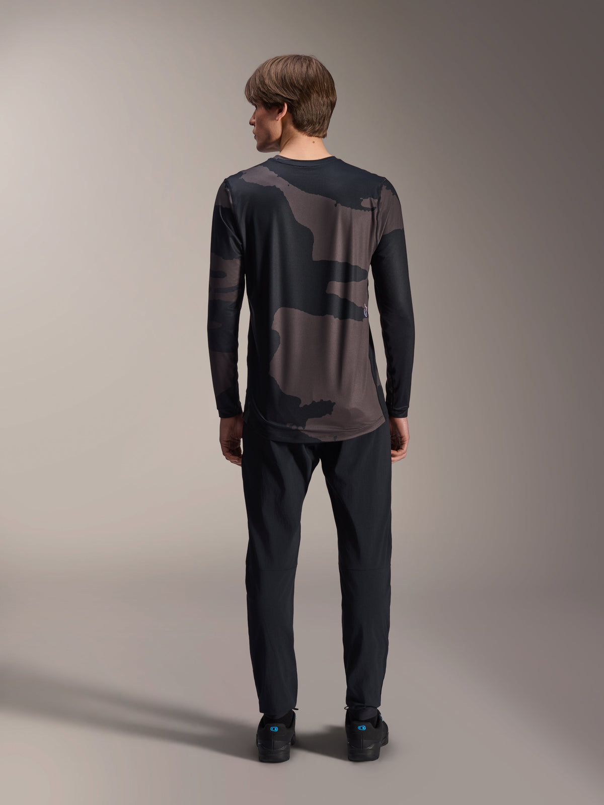Alpinestars A-Dura Hollow Camo Langarm-Trikot, Black Camo, Rückansicht getragen mit schwarzer Hose, mit dunklem Camouflage-Muster und verlängertem Rückensaum für MTB-Abdeckung.