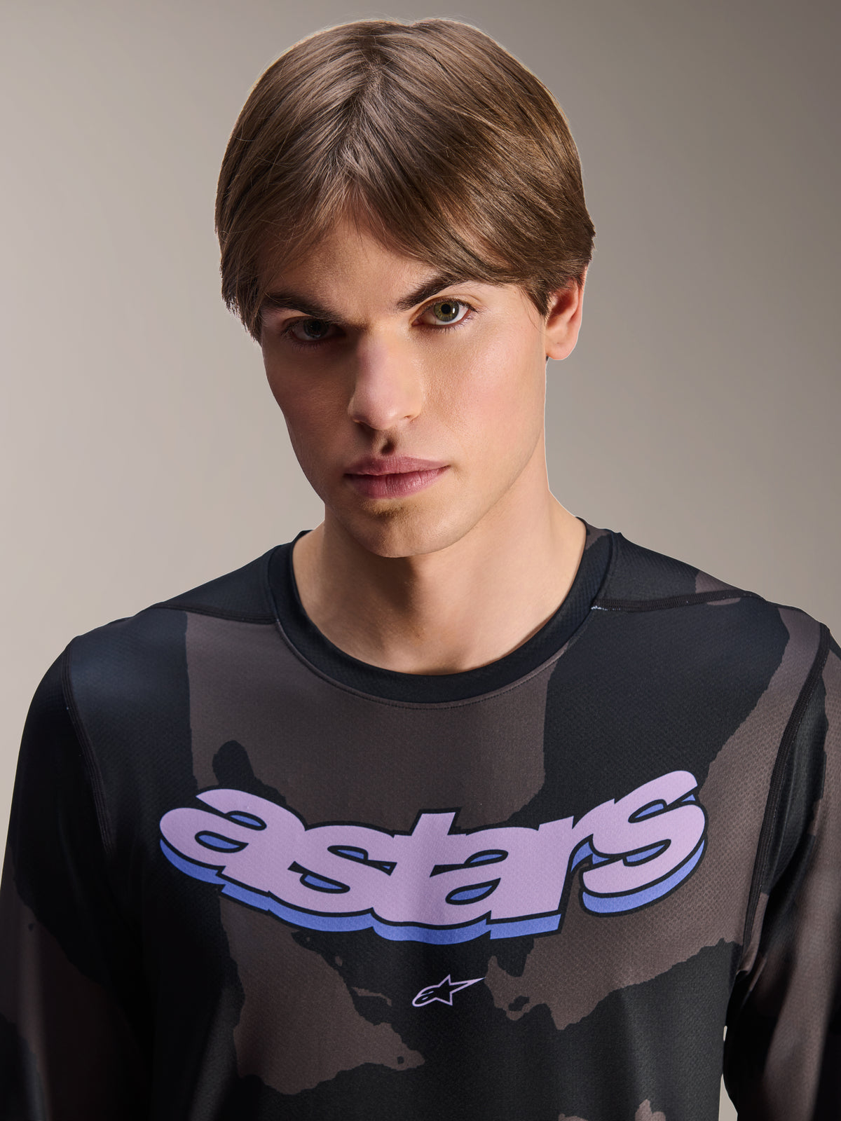 Alpinestars A-Dura Hollow Camo Jersey – Langarm, Schwarz-Camo mit lila 'astars' Grafik auf der Brust, Studioaufnahme eines männlichen Models in MTB-Bekleidung, lässiger und technischer Mountainbike-Stil
