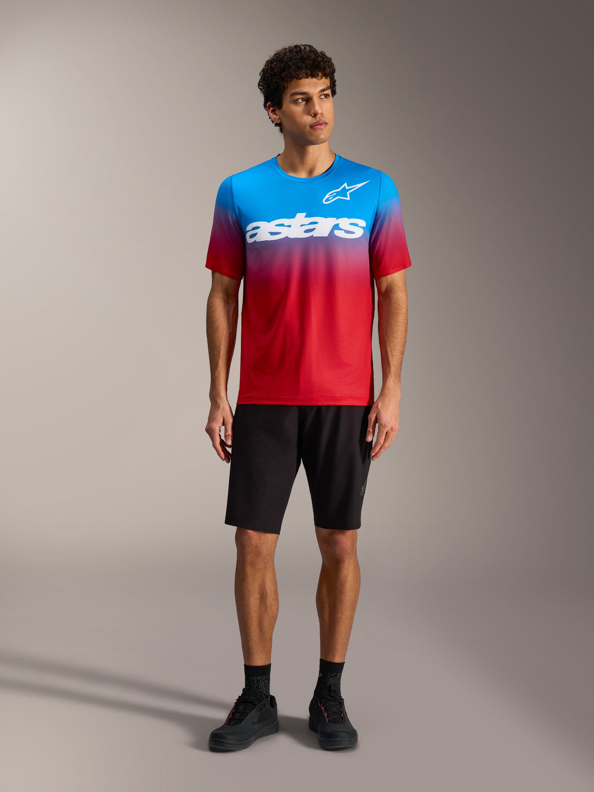 A-Dura ASTARS Jersey 2.0 met Bright Red Blue kleurverloop, wit logo, zwarte MTB-short en fietsschoenen.