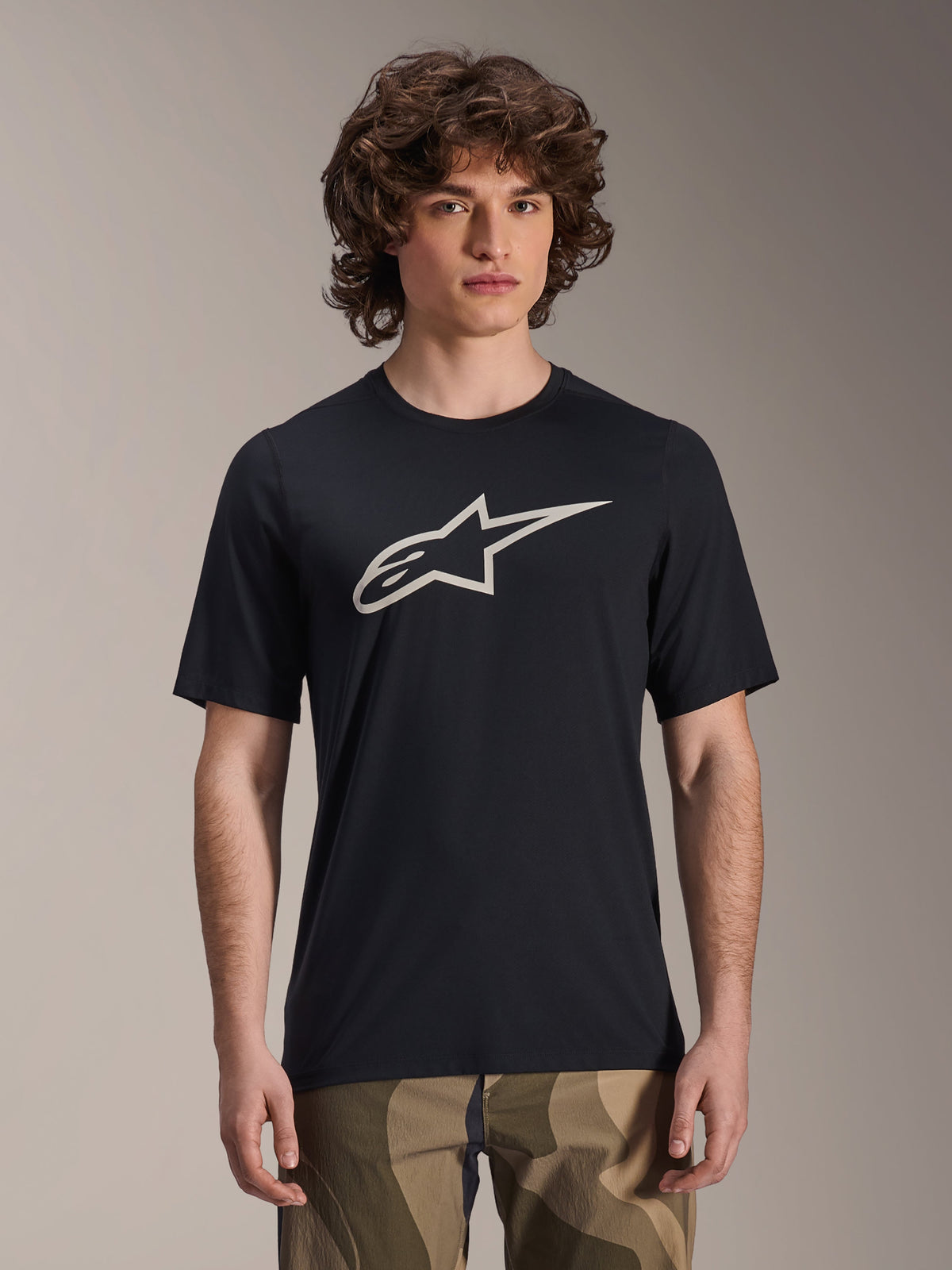 Alpinestars A-Dura Astar Jersey met korte mouwen, zwart MTB-shirt met wit sterlogo, gedragen met camouflagebroek, casual mountainbike-kleding, technische vochtafvoerende stof