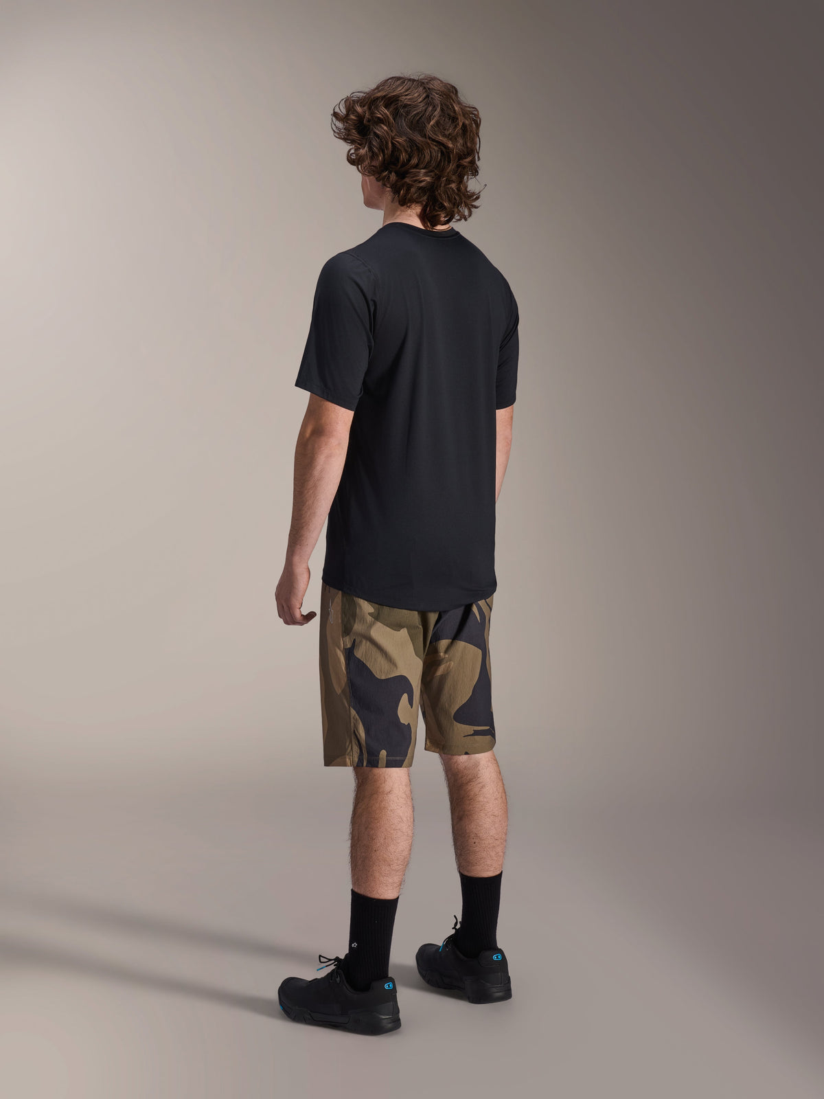 Alpinestars A-Dura Astar jersey met korte mouwen in het zwart, van achteren gezien, gecombineerd met een short met camouflagepatroon, zwarte sportsokken en schoenen, casual MTB-kleding