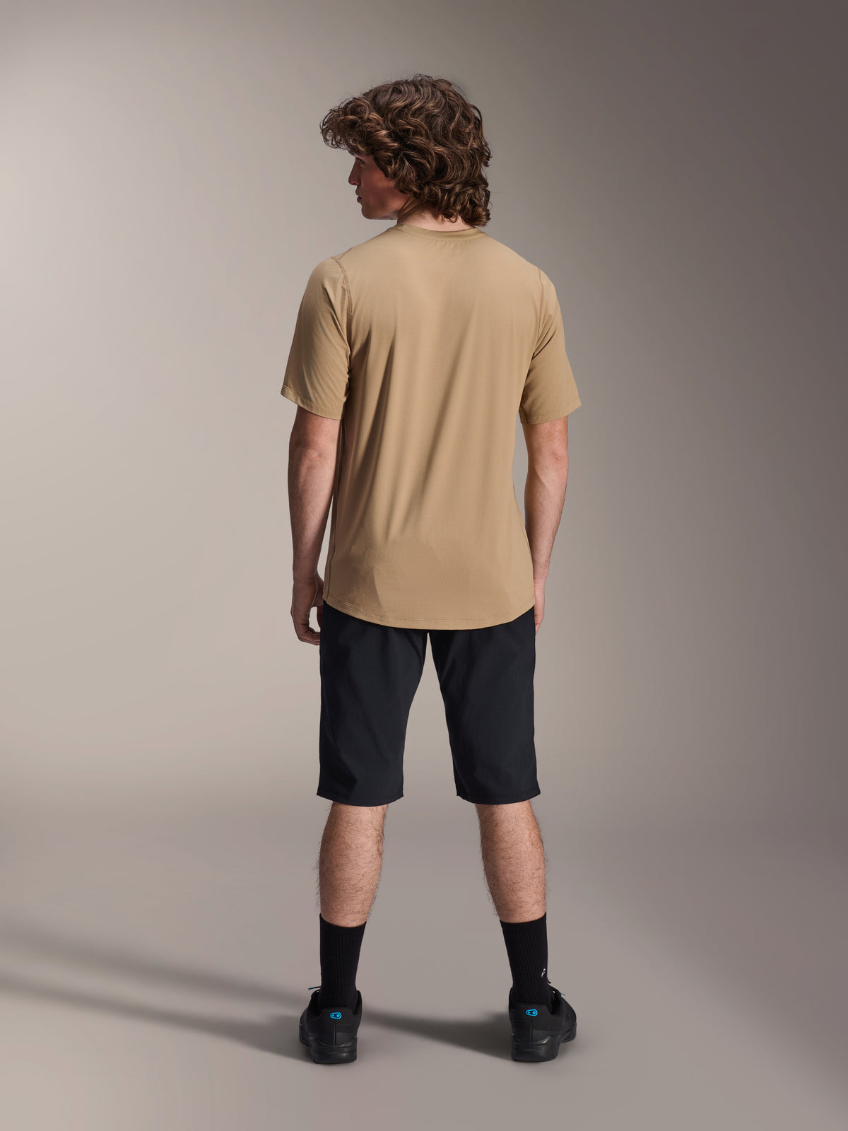 Mannelijk model van achteren gezien in Alpinestars A-Dura Liner Shorts in het zwart en een beige jersey met korte mouwen, gecombineerd met zwarte sokken en schoenen, duurzame mountainbikekleding voor off-road fietsen.