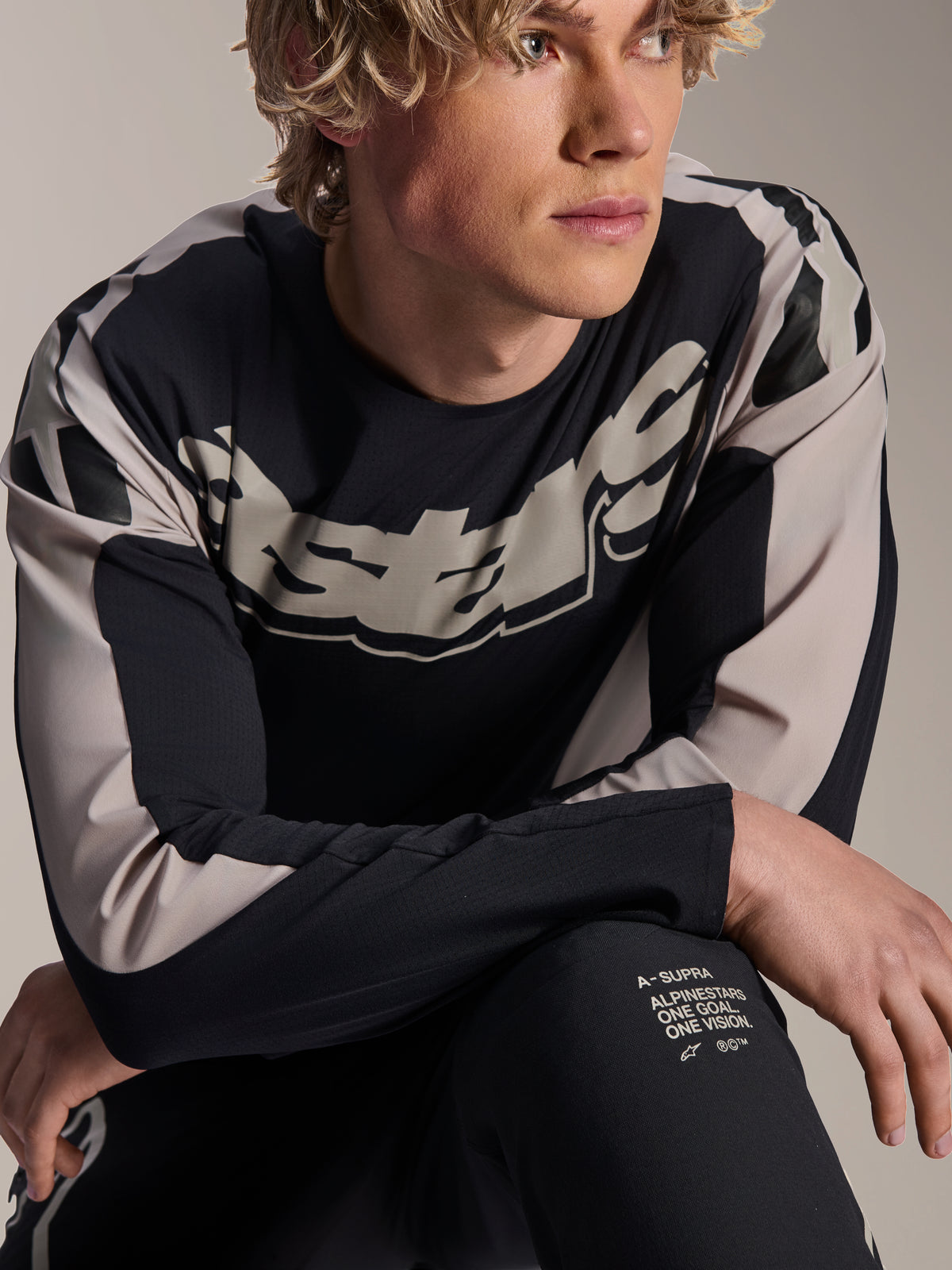 Maillot Alpinestars A-Supra Melt, maillot de VTT à manches longues, noir avec graphismes gris clair, porté par un mannequin, arborant un logo imposant sur la poitrine et l'inscription « One Goal. One Vision. », vêtement de performance pour le VTT
