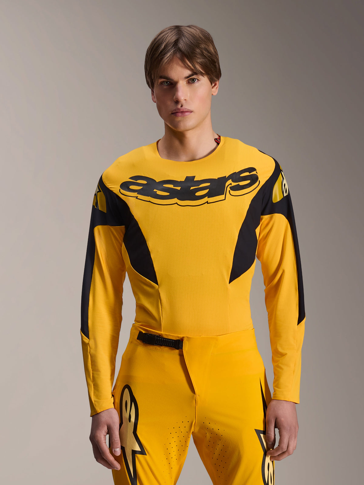 Alpinestars Limited Edition A-Supra Melt Gold Jersey, MTB-jersey met lange mouwen, donkergeel met zwarte accenten, gedragen door een model met bijpassende broek, voorzien van een groot zwart 'astars'-logo op de borst en een sportief prestatiegericht ontwerp